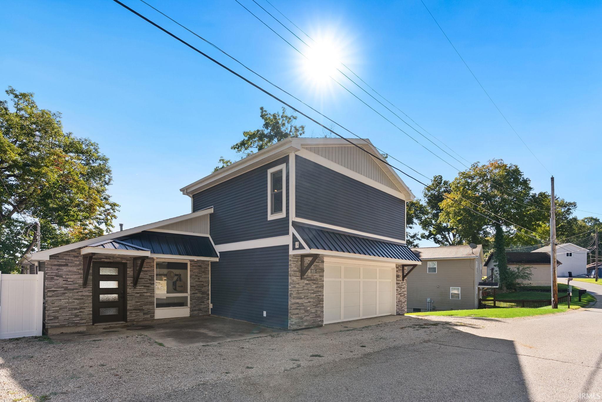 Contemporary exterior featuring dark blue siding, stone veneer accents, a white garage door, and a metal awning over the entrance