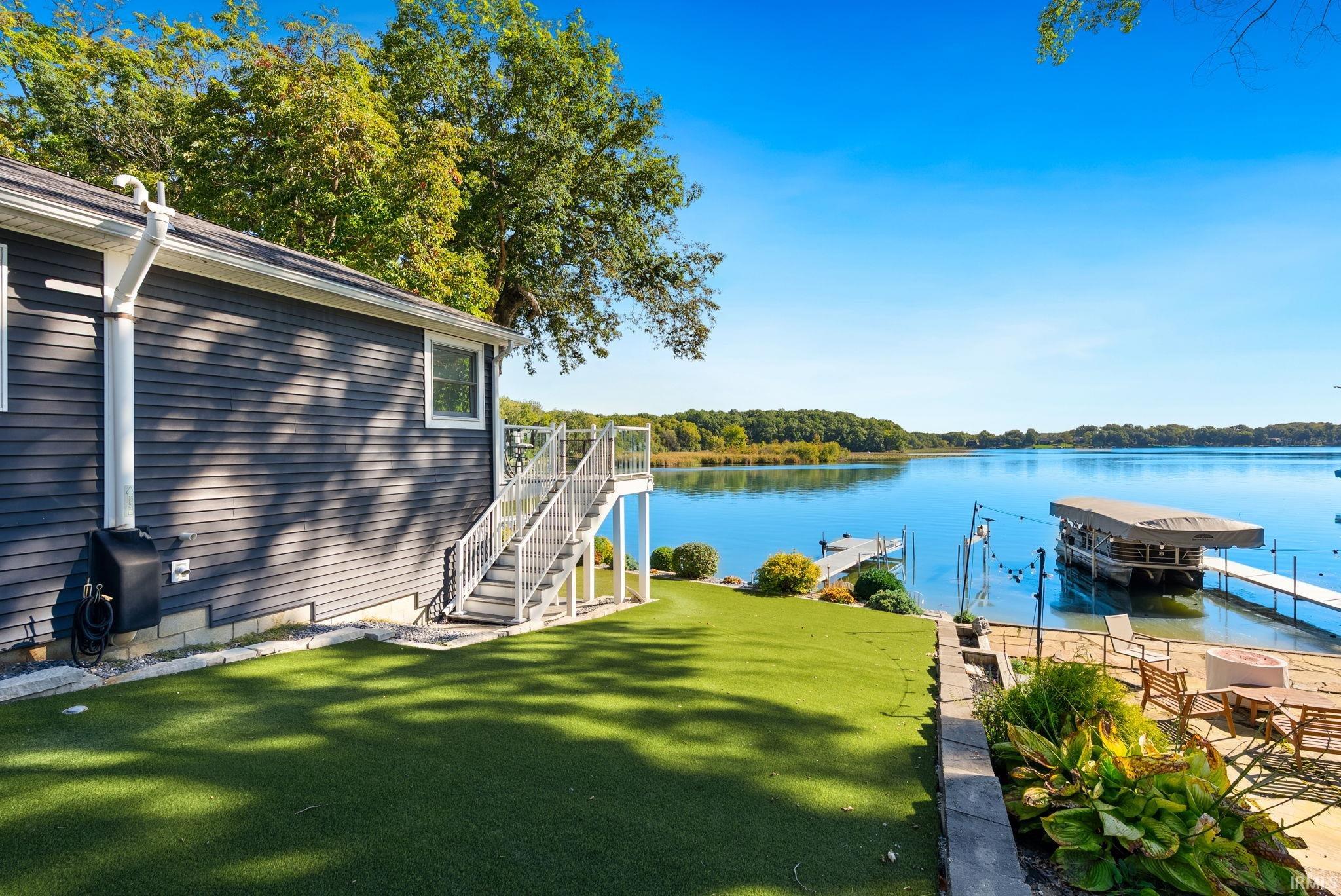 Lakeside property featuring an artificial turf lawn, an exterior staircase with glass panel railing, and multiple docks with boat lifts