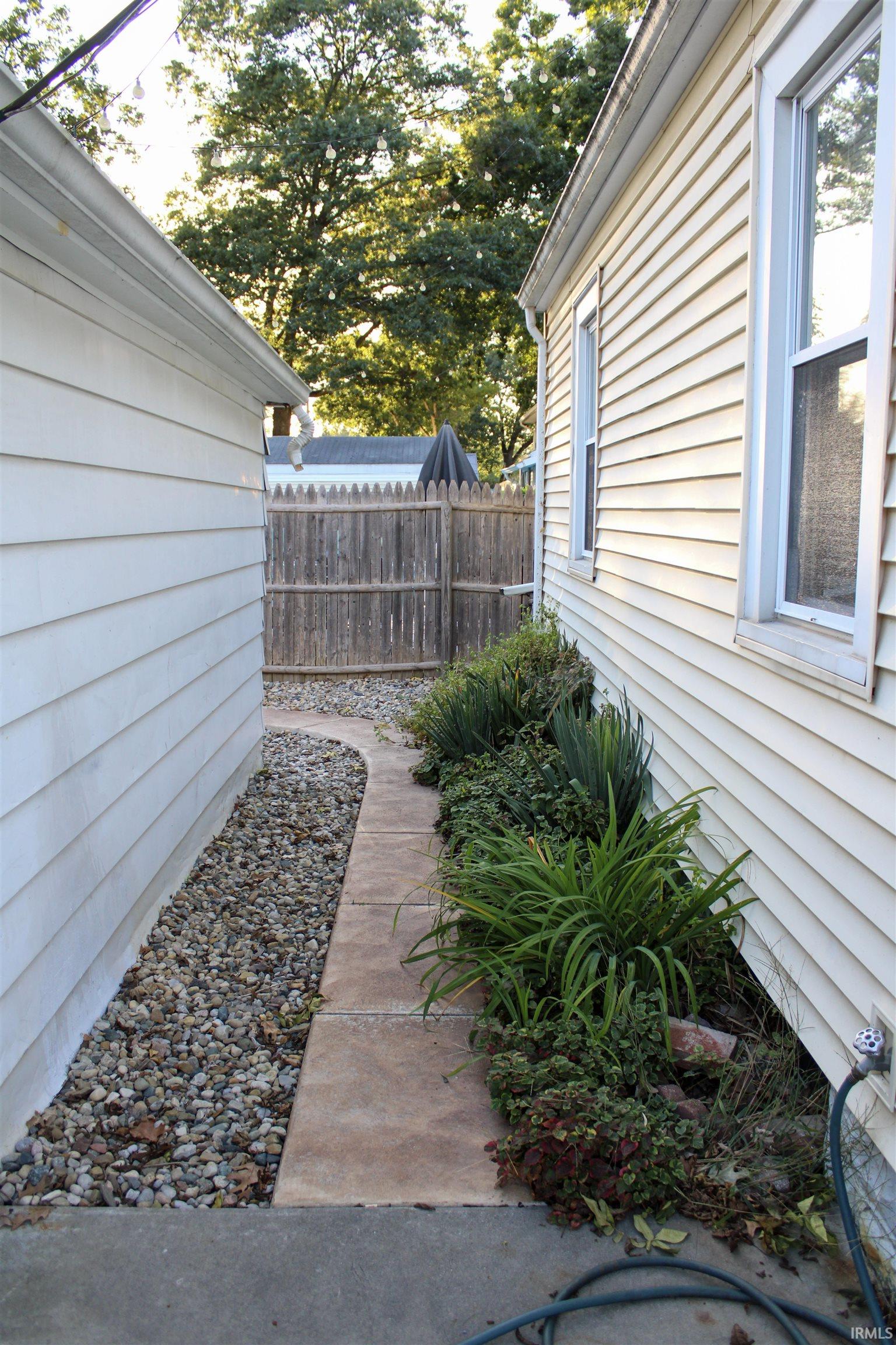 Siding exterior with multiple windows, concrete walkway, gravel landscape, and planted greenery