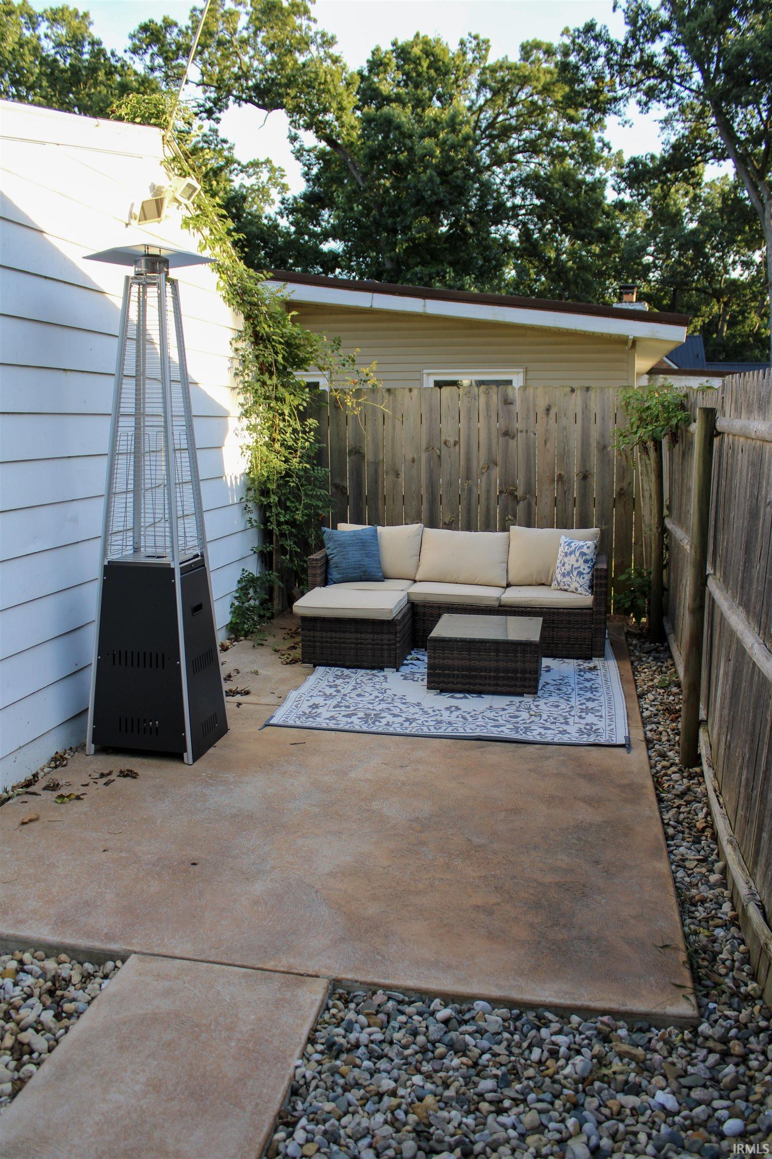 Concrete patio with a pebble border, bordered by a wood fence, and featuring established perimeter plantings