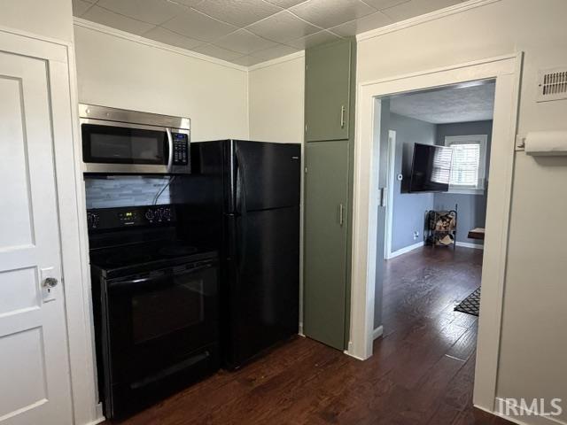 Stainless steel microwave, black electric range, black refrigerator, green built-in cabinetry, and wood-finish flooring