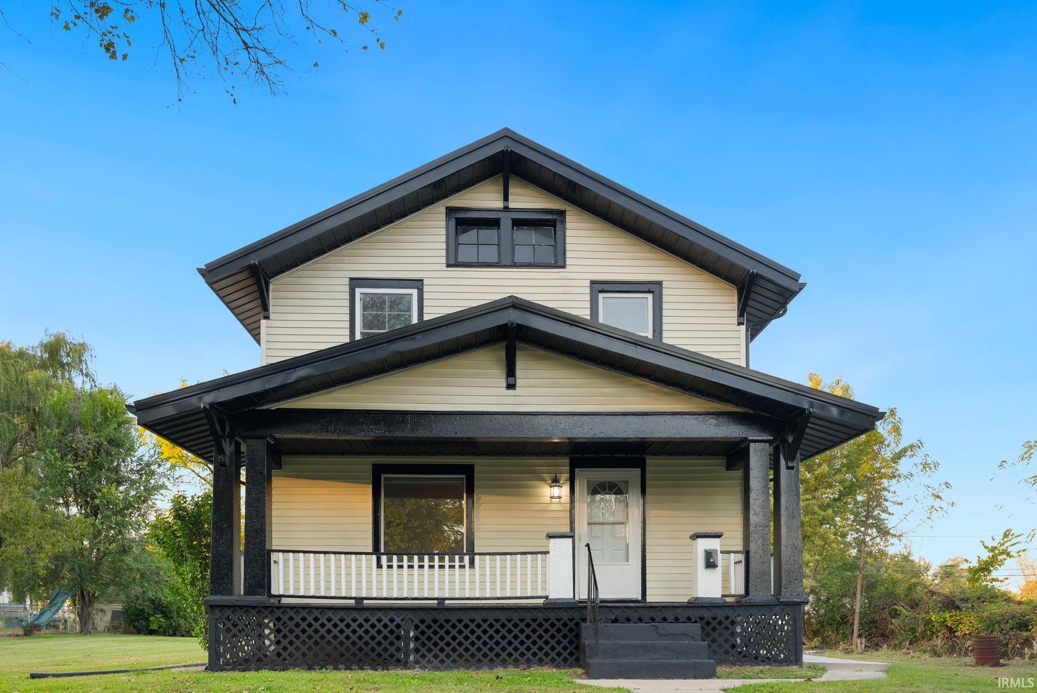 Two-story residence featuring horizontal siding, a covered front porch with lattice skirting, decorative gable brackets, and a dual-gabled roofline