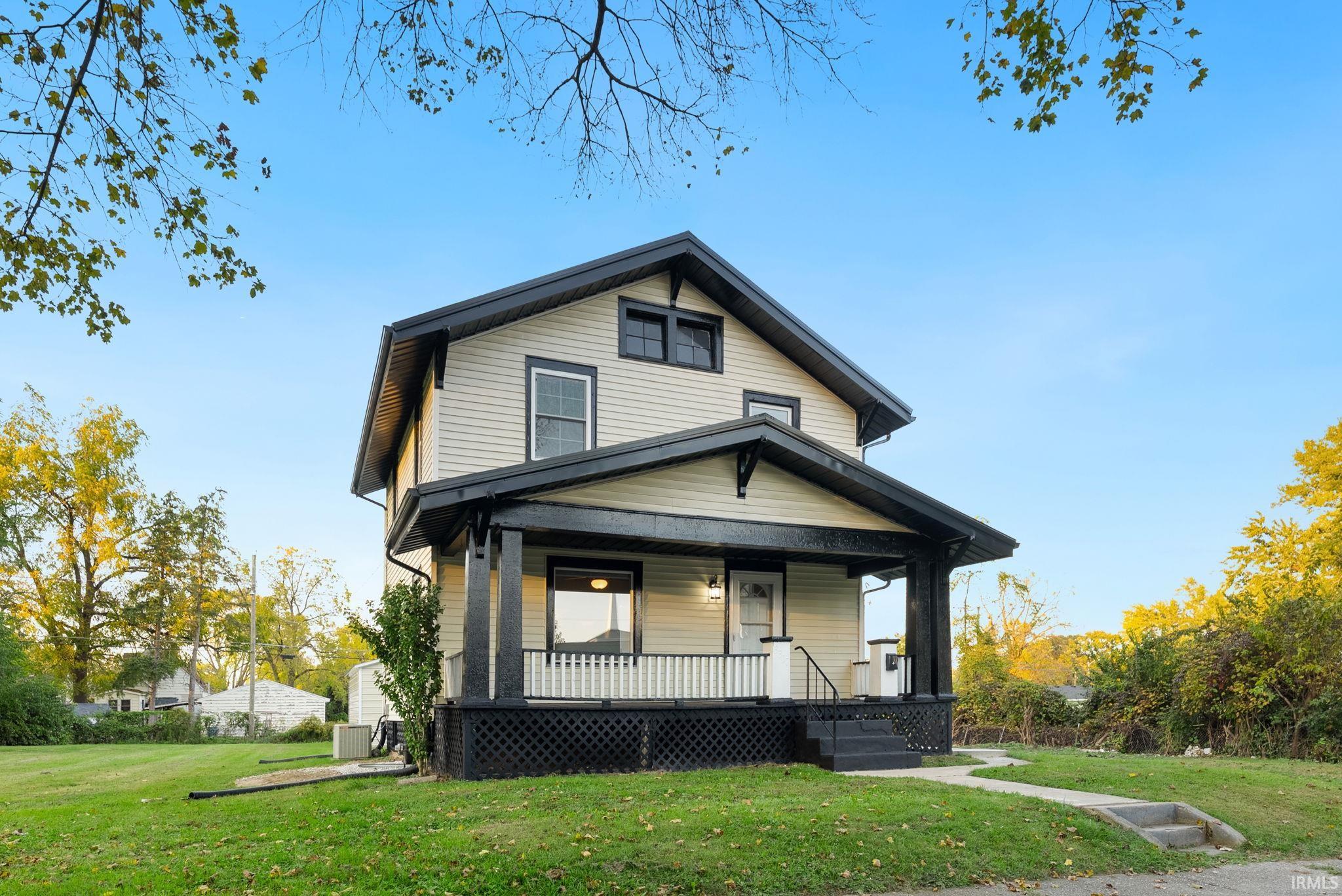 Two-story home with horizontal siding, a covered front porch featuring decorative lattice skirting, dark structural trim, and a gable roofline