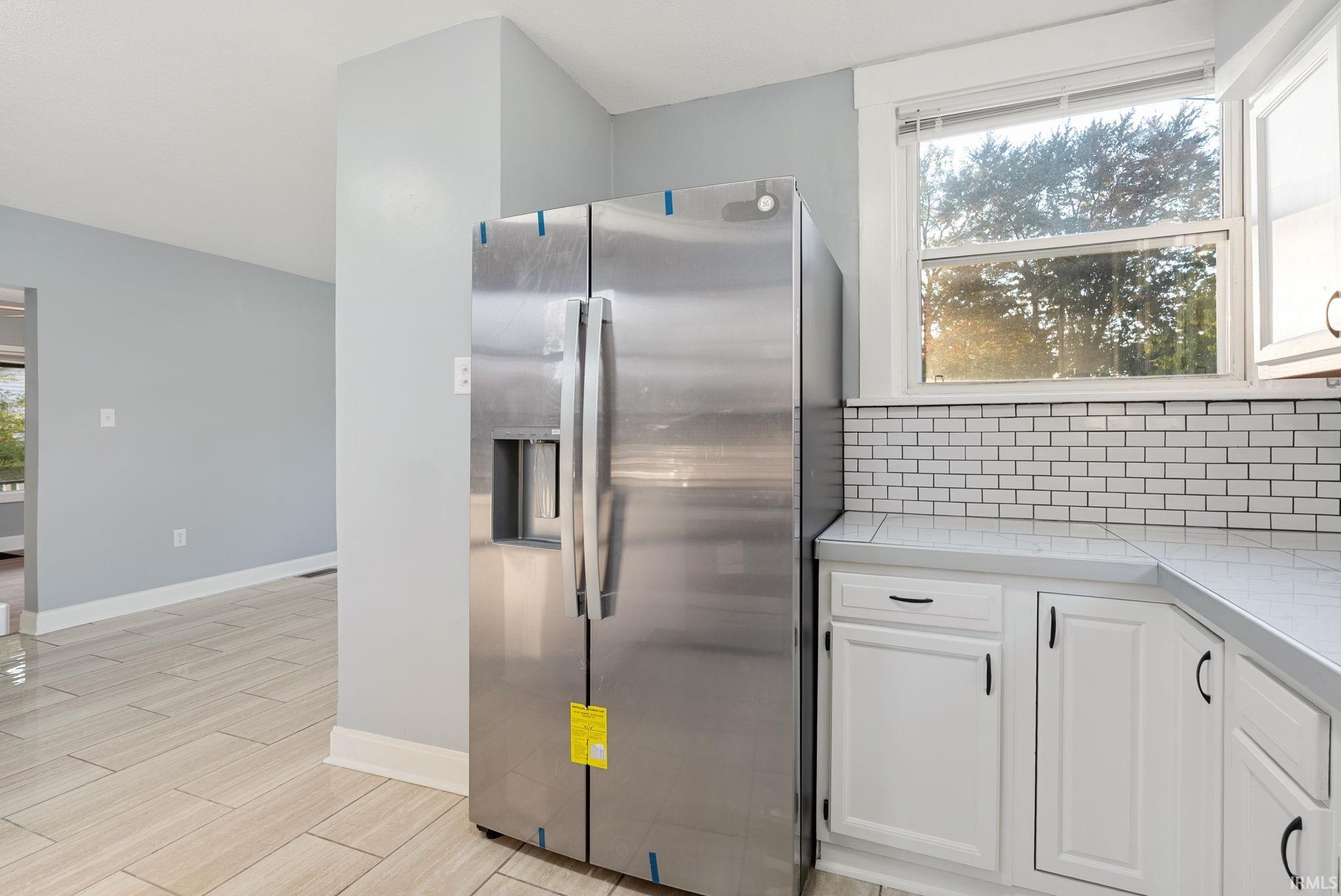 Kitchen area featuring stainless steel refrigerator, white cabinetry, subway tile backsplash, and light-toned tile flooring