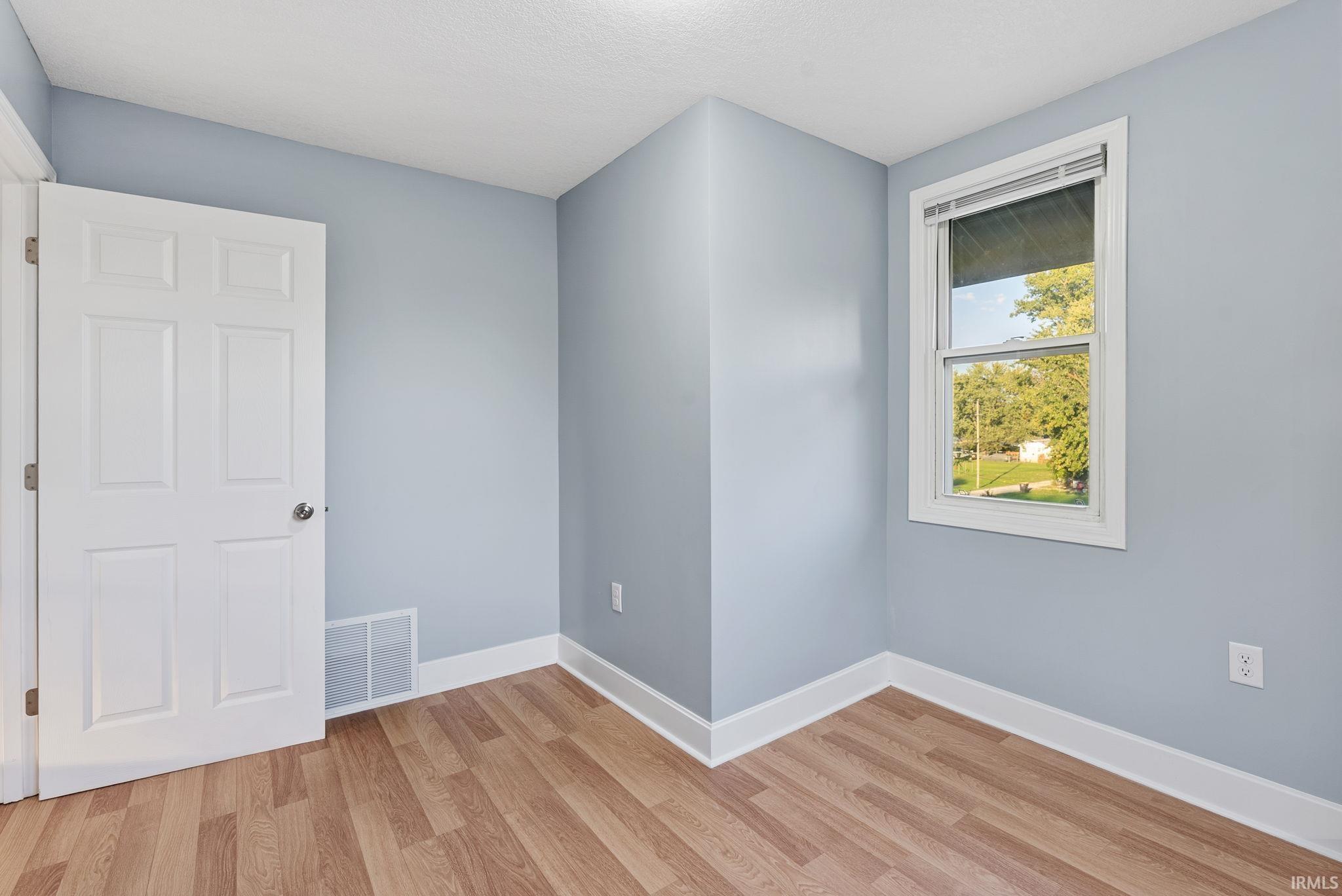 Interior room featuring wood-finish flooring, a single-hung window, and a multi-panel door