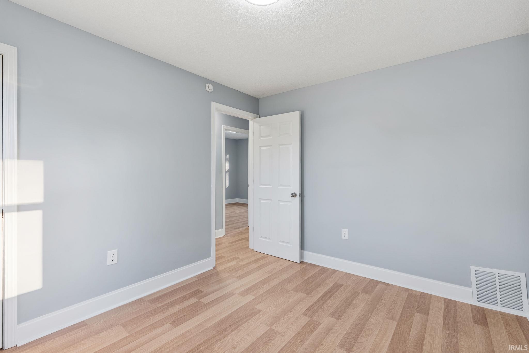 Neutral-toned interior room featuring wood-finish flooring, six-panel interior doors, and white-painted casing