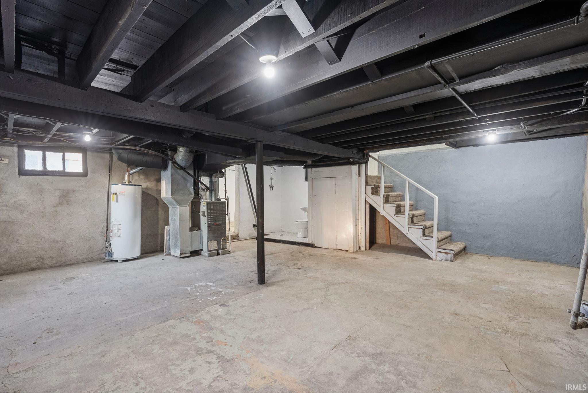 Lower level featuring painted exposed ceiling joists, concrete flooring, masonry walls, a utility water heater, and a staircase with a white railing