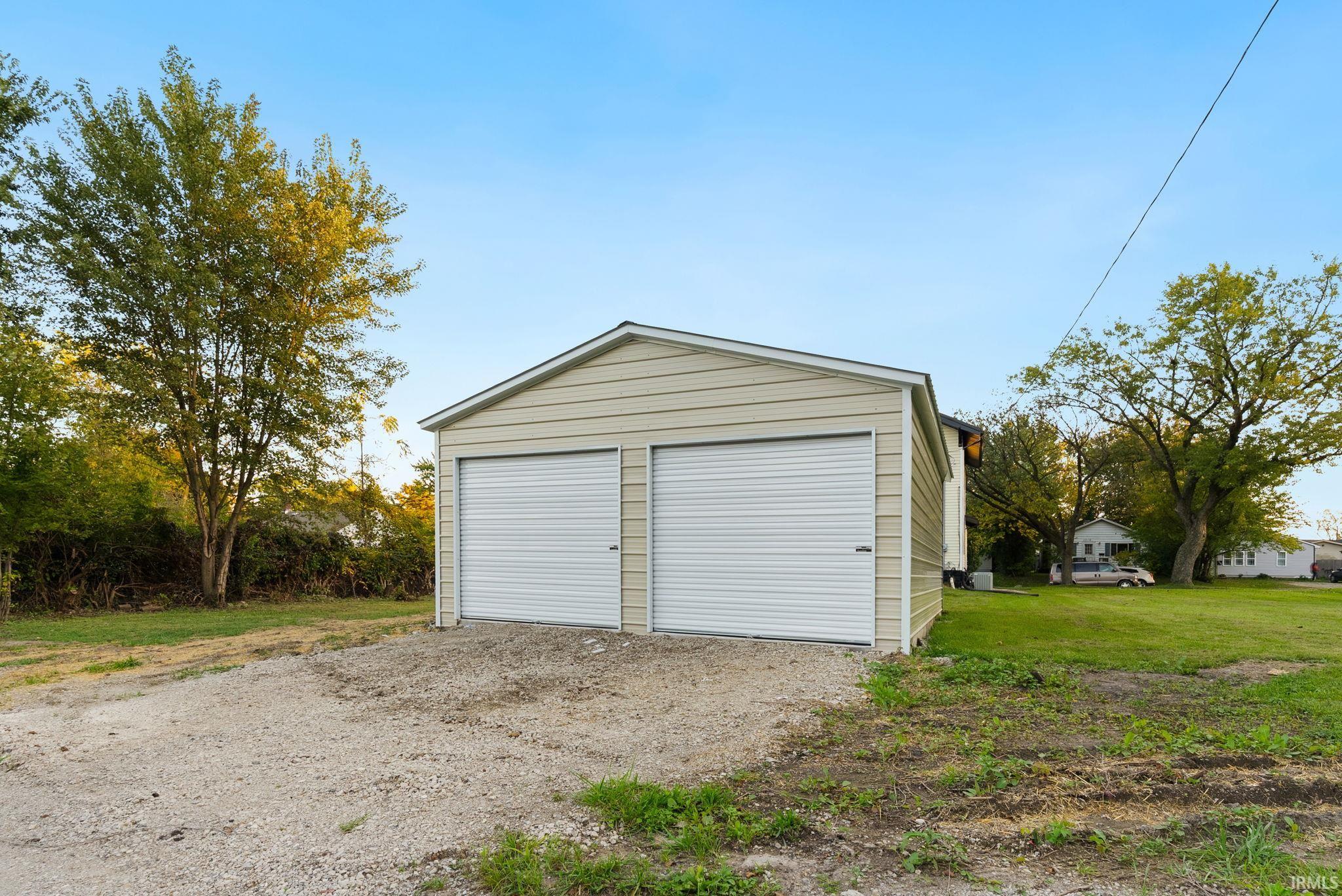 Detached two-car garage featuring light-toned horizontal siding, dual metal roll-up doors, and a gravel driveway