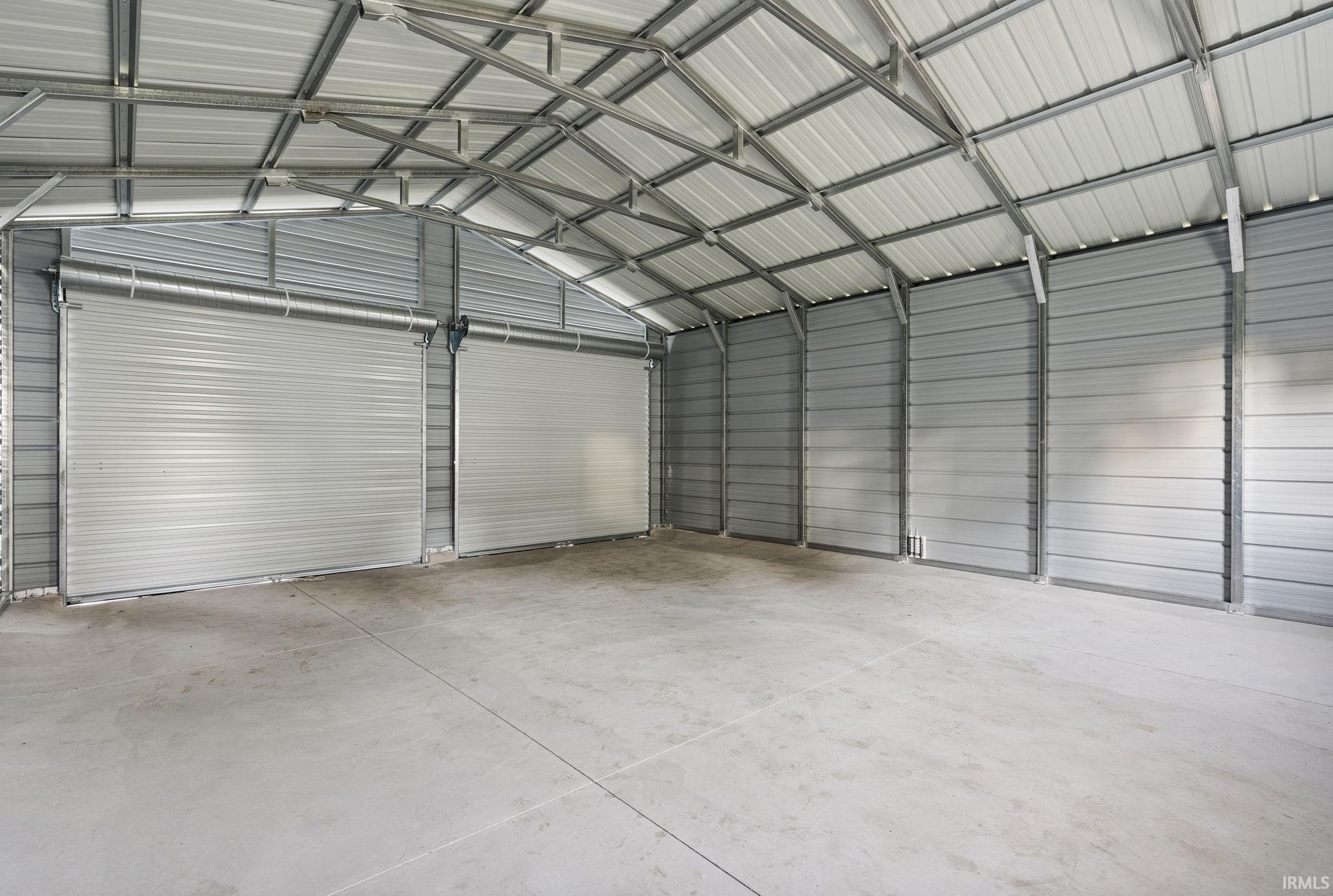 Spacious detached garage featuring a concrete slab floor, metal siding, a metal roof structure, and two roll-up doors
