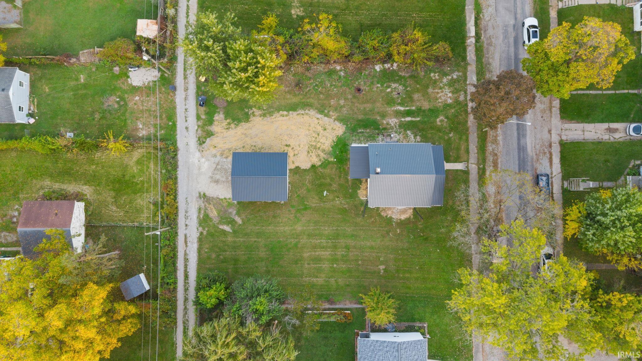 Aerial perspective of the property featuring a rectangular lot, detached structure, main residence with a dark-toned roof, and expansive lawn area