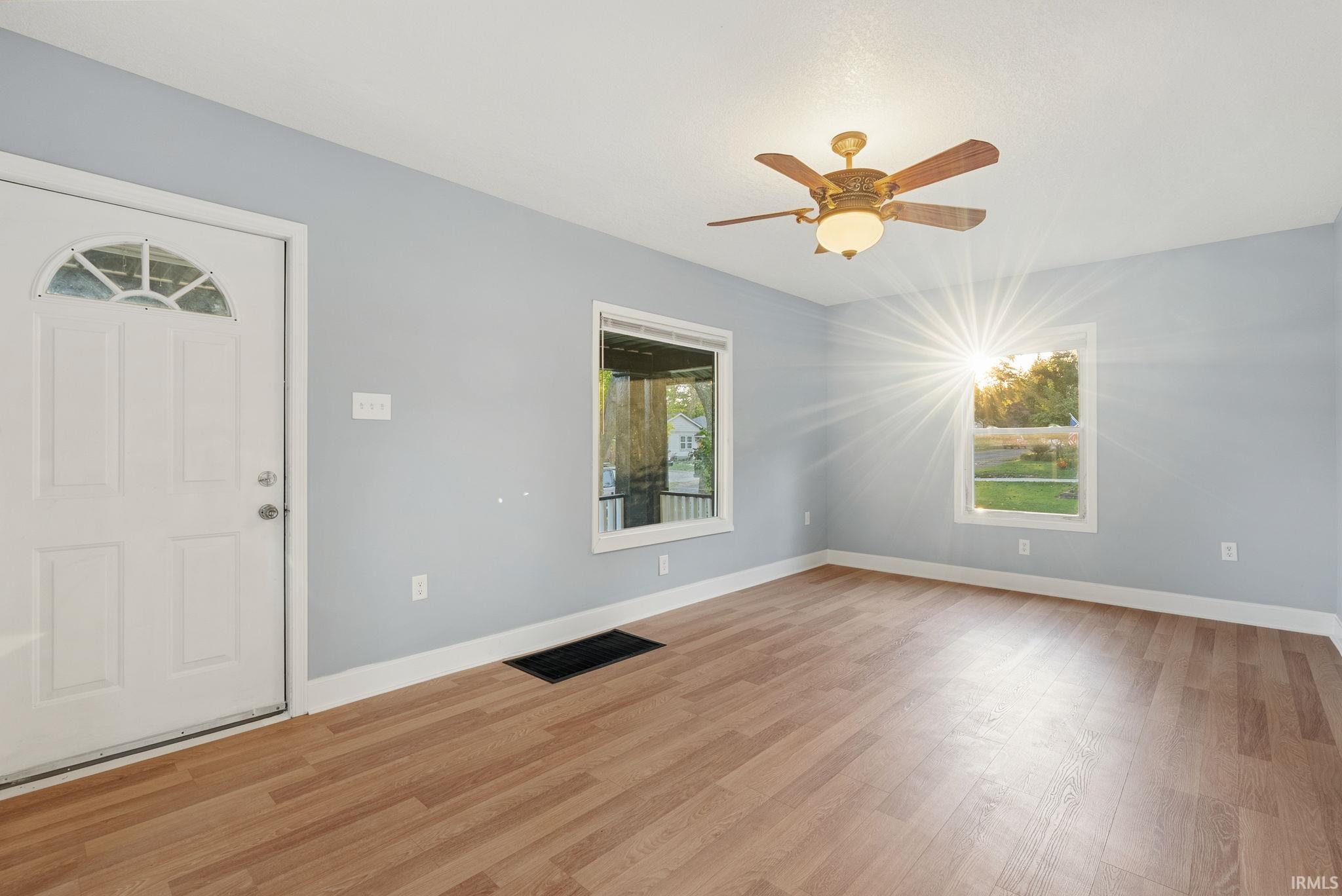 Interior space featuring wood-finish flooring, a ceiling fan with integrated lighting, and a six-panel exterior door with a semi-circular transom window