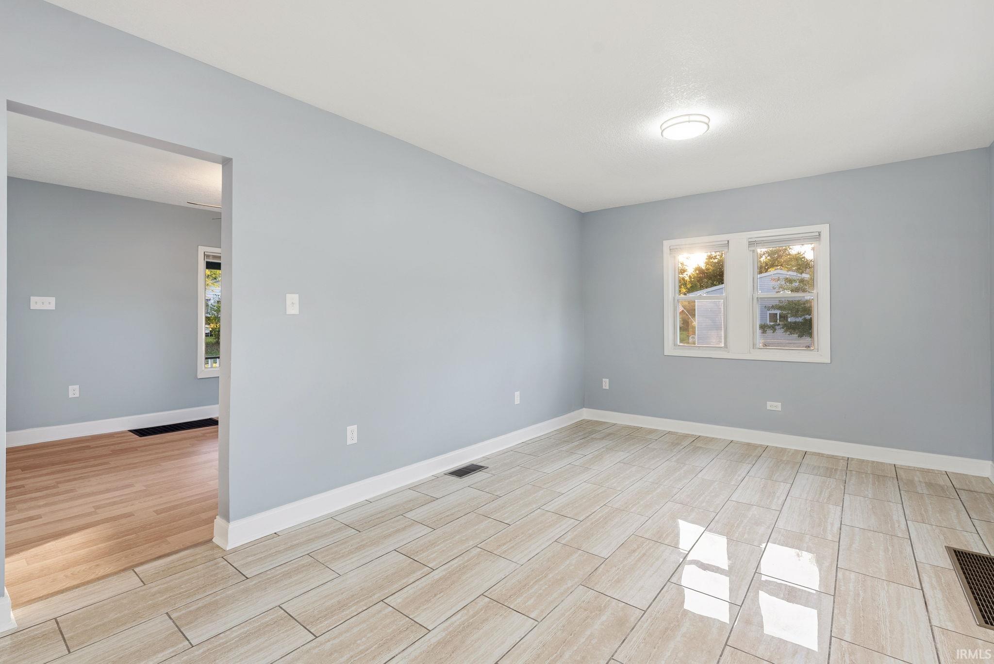 Interior space featuring large-format neutral tile flooring, light grey wall paint, and natural wood-finish flooring in the secondary room