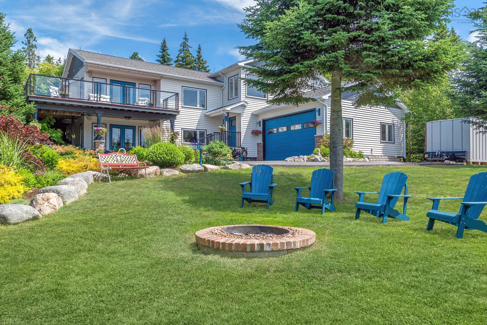 116 Whitecap Ridge, Black Point, NS (MLS® 202618413) — Expansive rear lawn featuring a brick-ringed fire pit, mature evergreen trees, and a terraced garden with natural stone accents