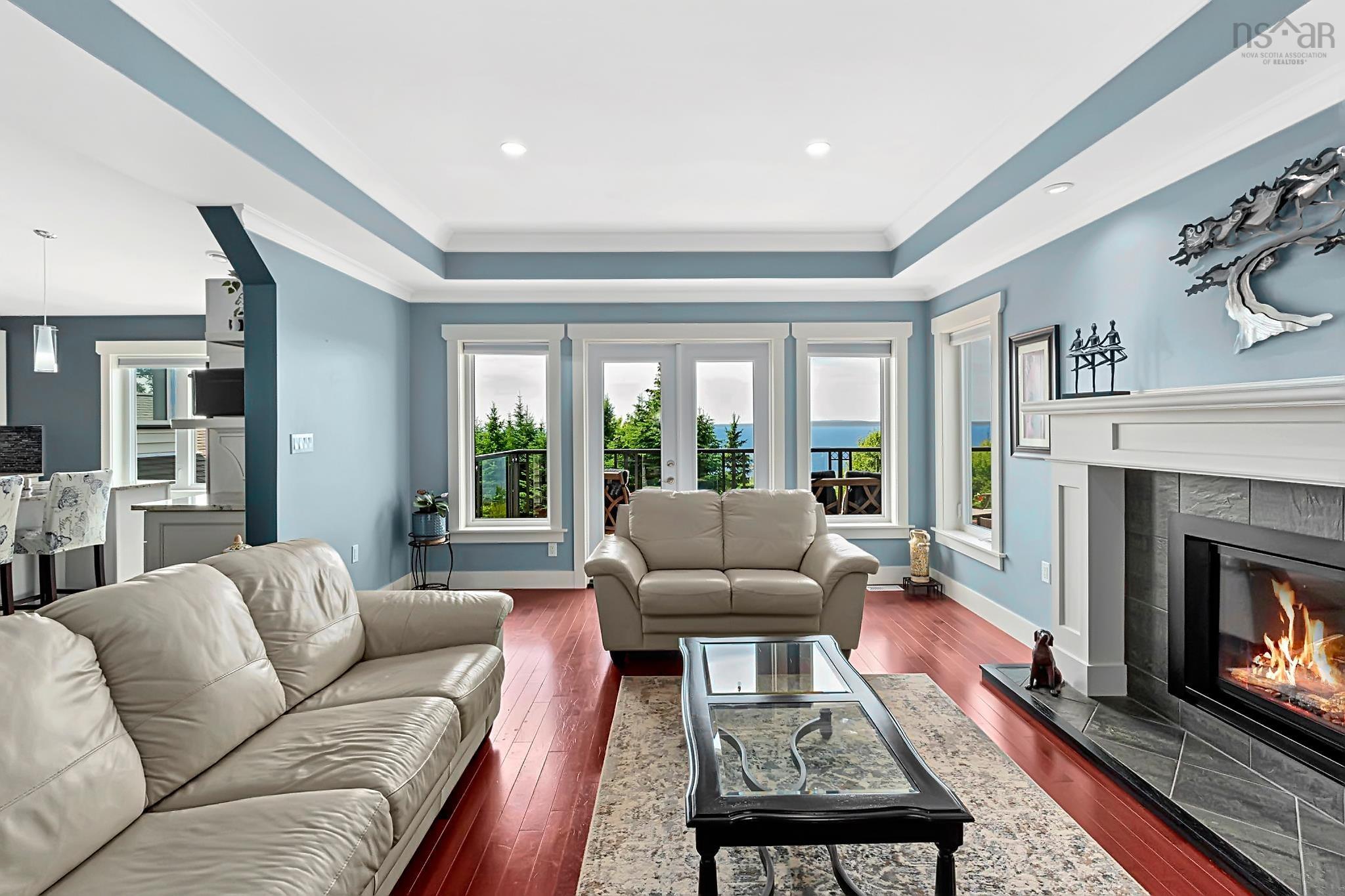 116 Whitecap Ridge, Black Point, NS (MLS® 202618413) — Living room featuring rich wood-finish flooring, a tray ceiling with recessed lighting, and a fireplace with a tiled hearth and mantel