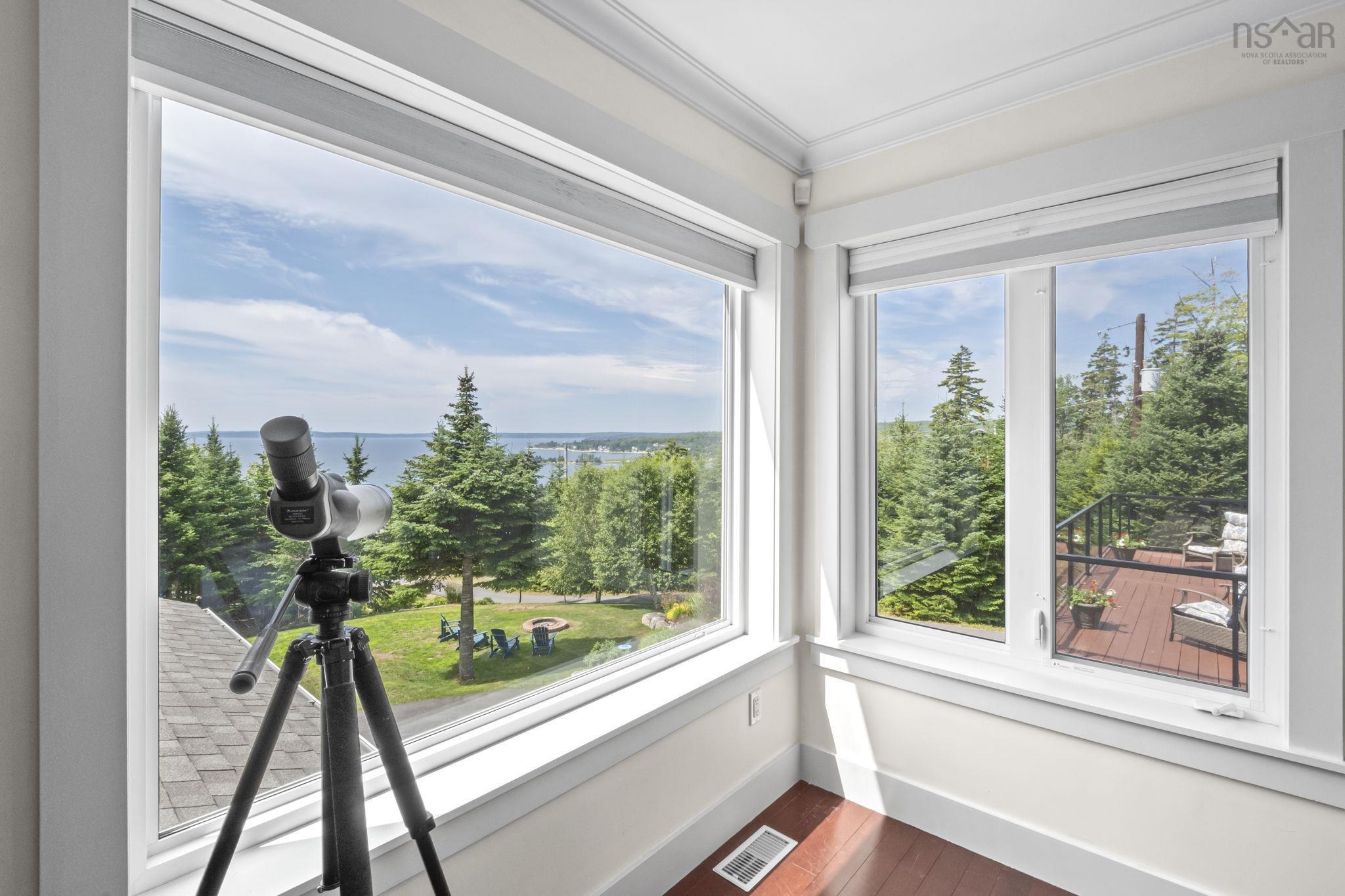 116 Whitecap Ridge, Black Point, NS (MLS® 202618413) — Corner window arrangement with crown molding, offering expansive water scenery, mature trees, and a ground-level fire pit area