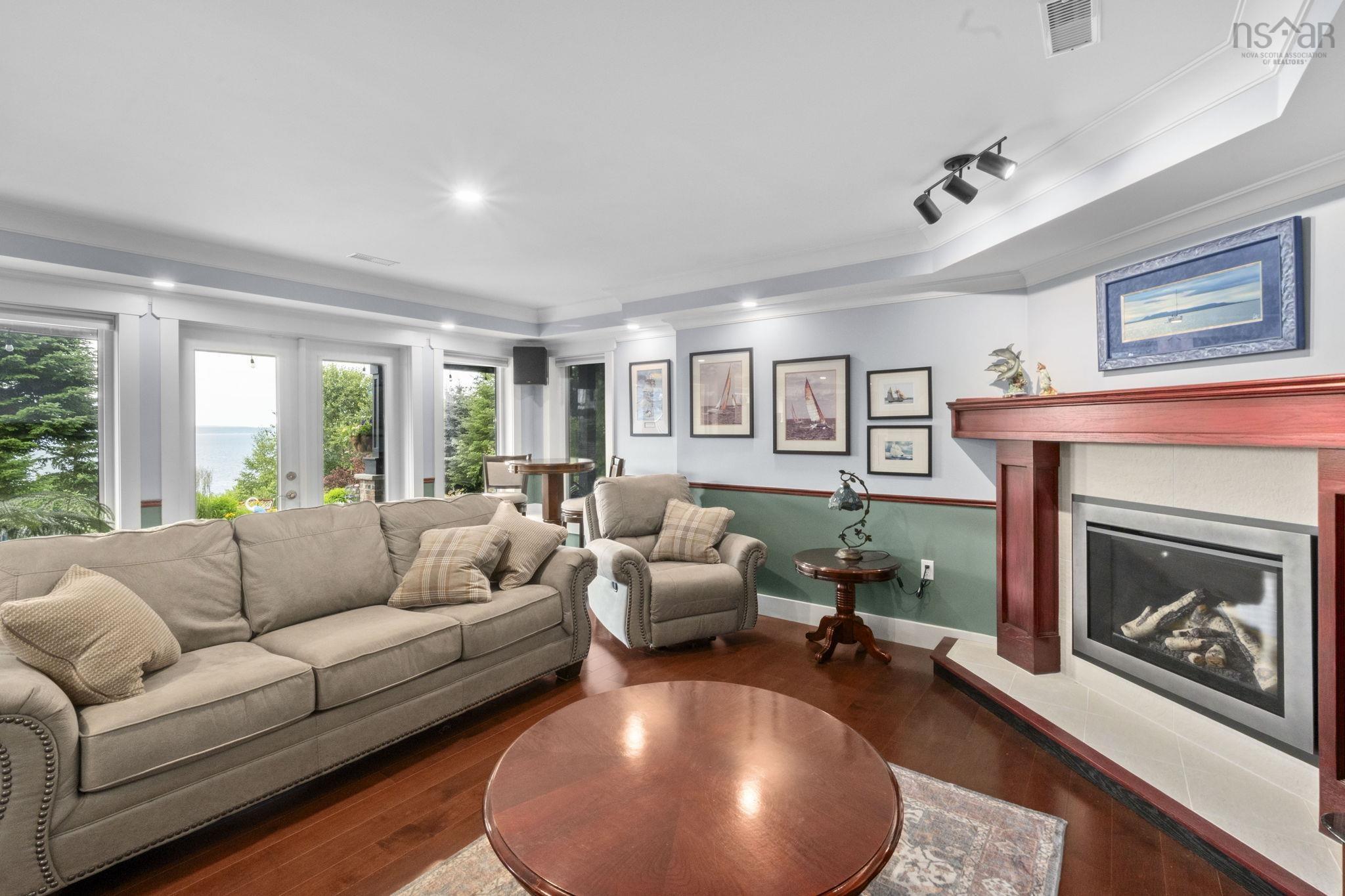 116 Whitecap Ridge, Black Point, NS (MLS® 202618413) — Living area with wood-finish flooring, a fireplace featuring a wood mantel, and multiple windows offering an expansive water view