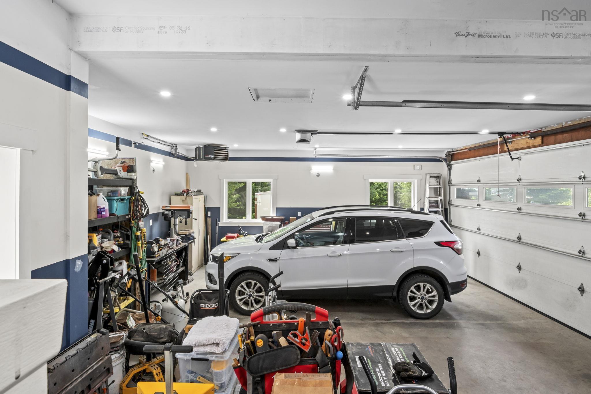 116 Whitecap Ridge, Black Point, NS (MLS® 202618413) — Spacious garage featuring a concrete floor, two overhead doors with window panels, multiple recessed ceiling lights, and additional wall sconces
