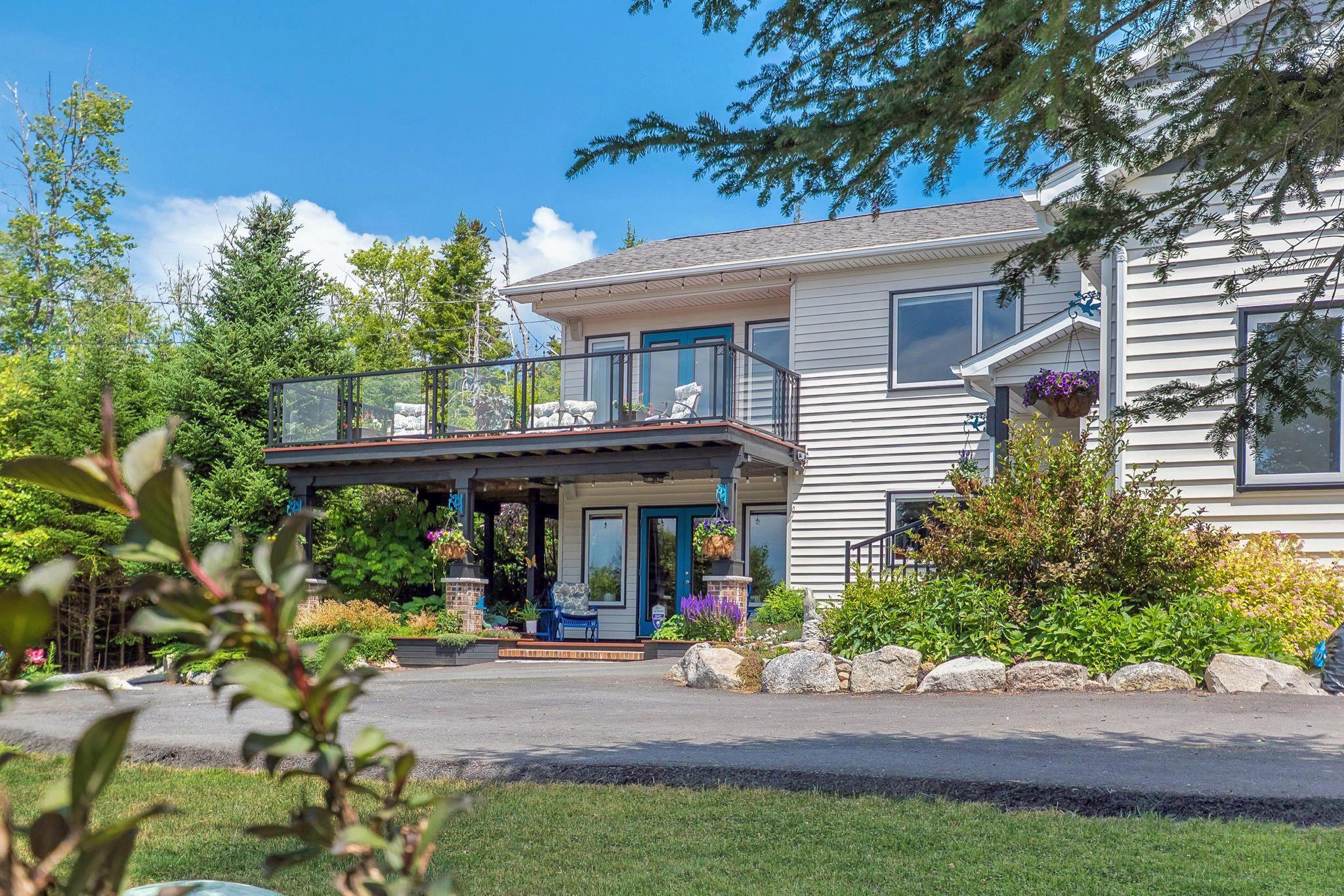 116 Whitecap Ridge, Black Point, NS (MLS® 202618413) — Two-story residence featuring light-toned horizontal siding, a second-level deck with glass panel railings, and a ground-level covered patio
