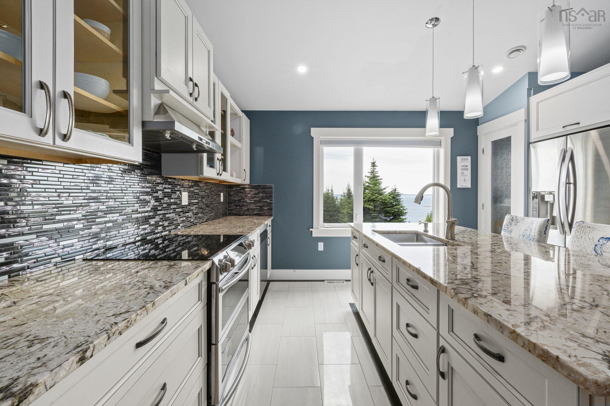 116 Whitecap Ridge, Black Point, NS (MLS® 202618413) — Modern kitchen featuring white cabinetry, granite countertops, a textured tile backsplash, a stainless steel refrigerator, and an integrated kitchen island with a double basin sink