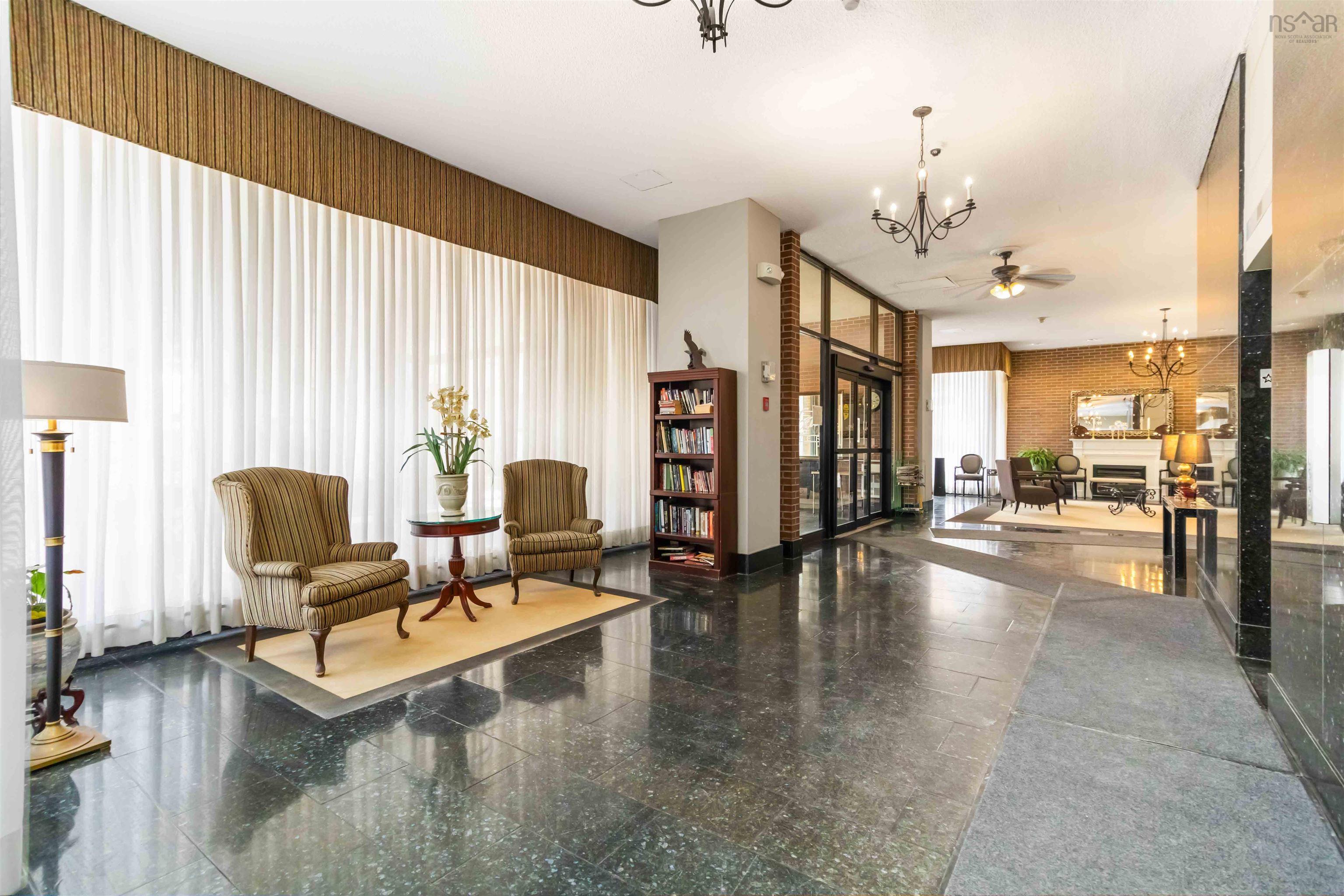 1601 5959 Spring Garden Road, Halifax, NS (MLS® 202620845) — Polished dark stone flooring throughout, featuring a built-in bookshelf, full-height window treatments, and a brick wall accent