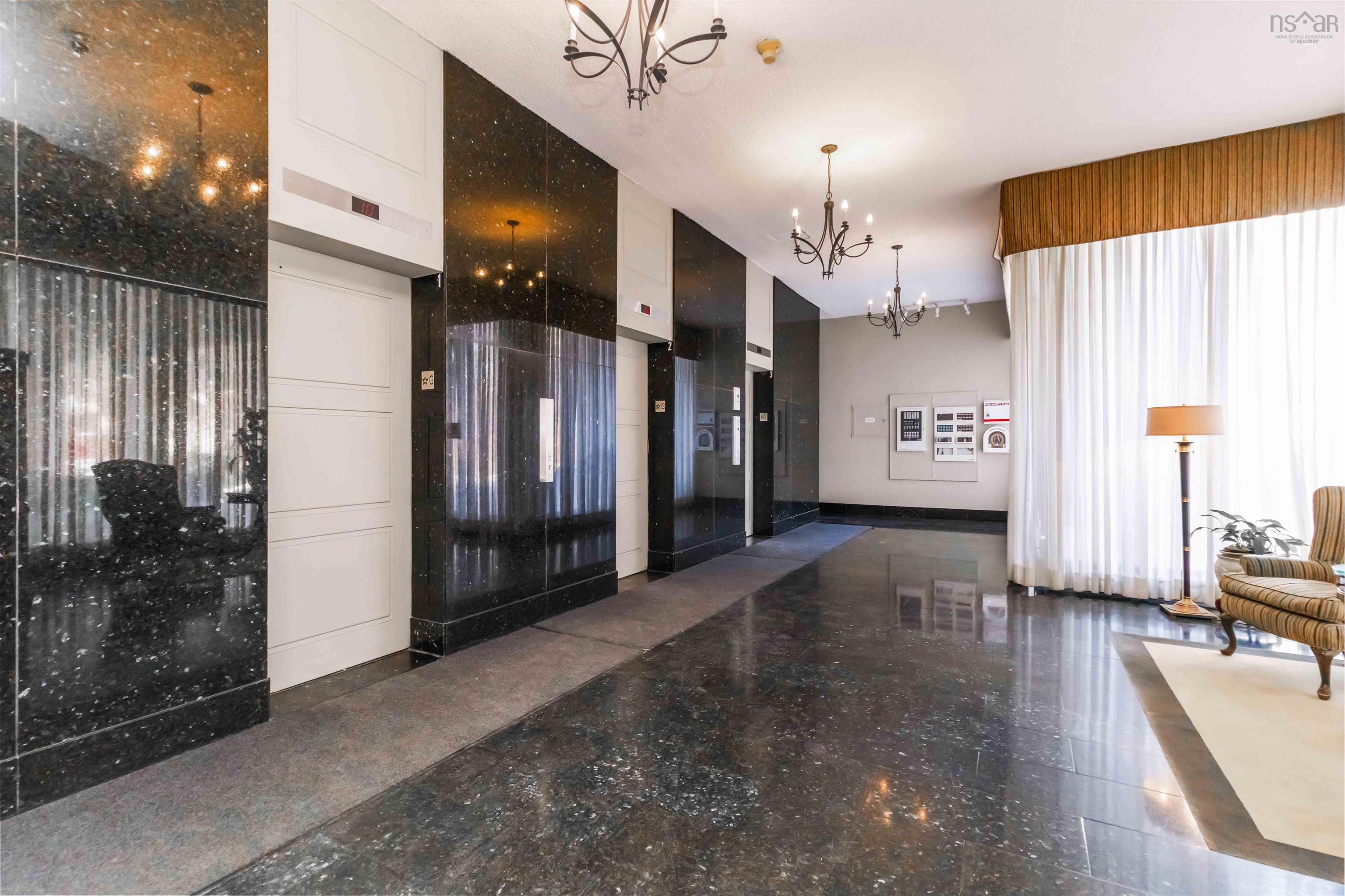 1601 5959 Spring Garden Road, Halifax, NS (MLS® 202620845) — Polished dark stone flooring, dark stone wall cladding, white paneled elevator doors, multiple chandeliers, and full-height white drapery