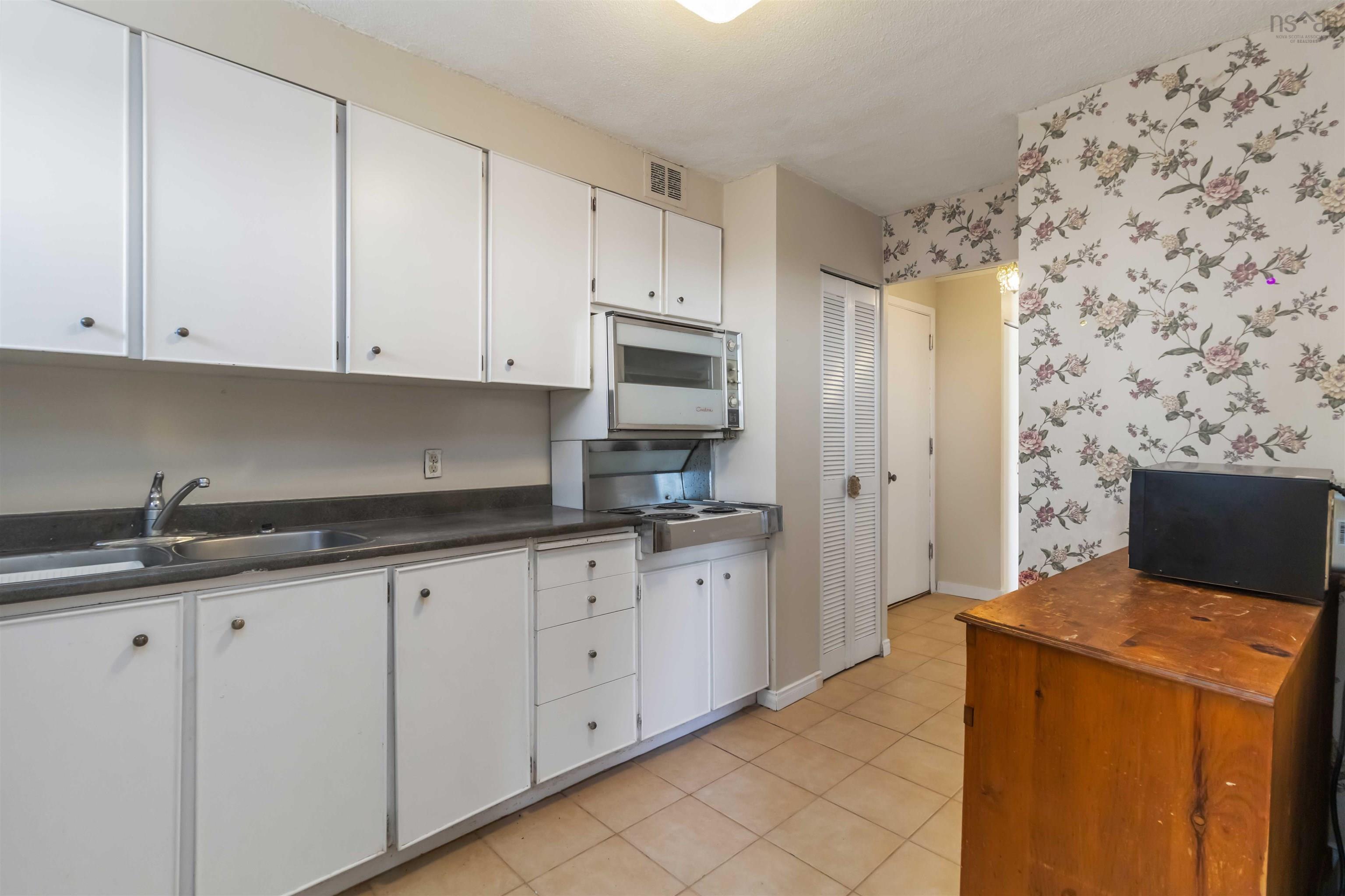 1601 5959 Spring Garden Road, Halifax, NS (MLS® 202620845) — White cabinetry with dark hardware, stainless steel sink, built-in microwave, tile flooring, and floral pattern wallpaper