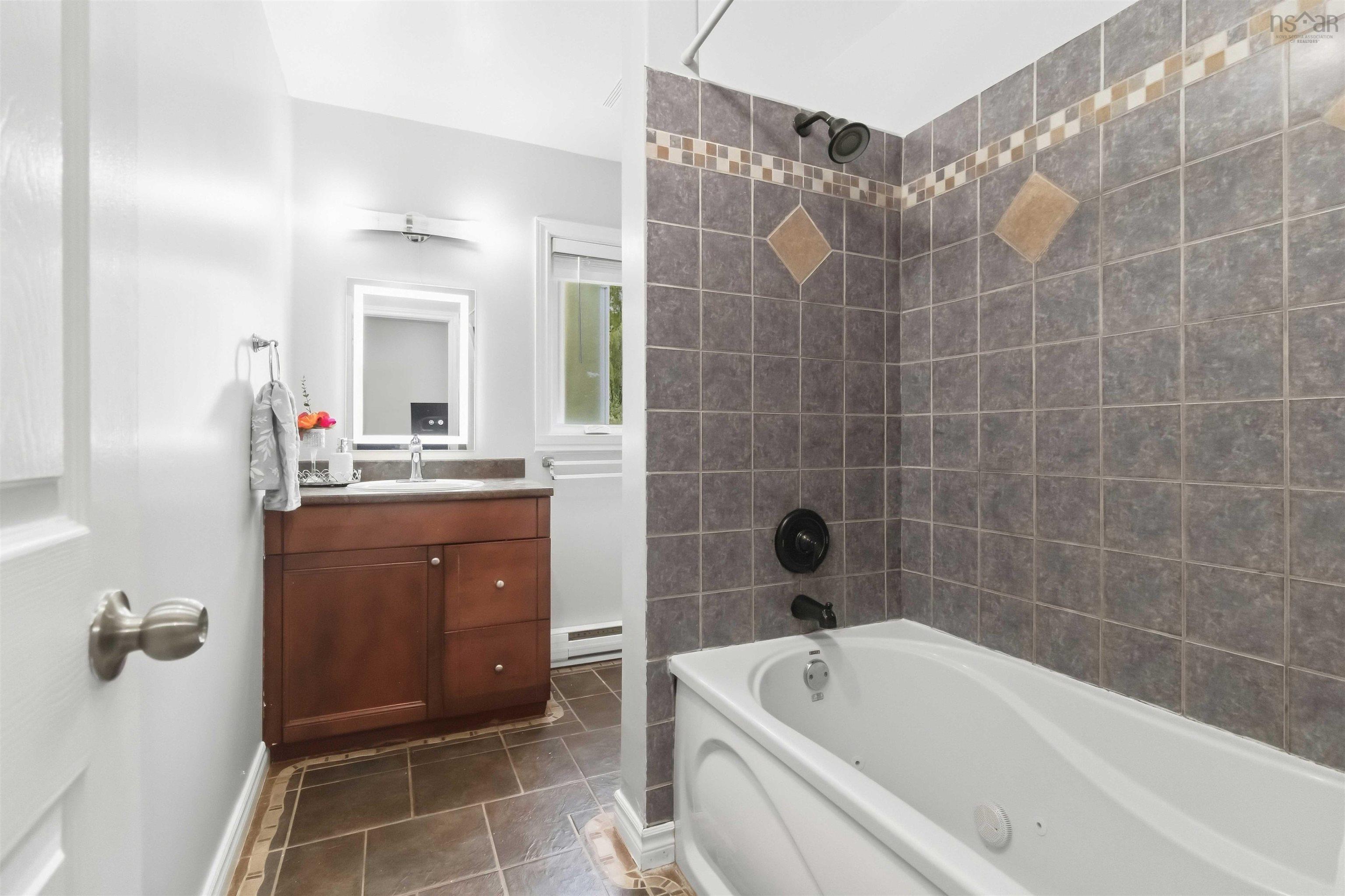 34 Lindsay Court, Lower Sackville, NS (MLS® 202624063) — Bathroom featuring a tiled tub surround with accent tiles, a white bathtub, a wood-finish vanity with a countertop, and tile flooring