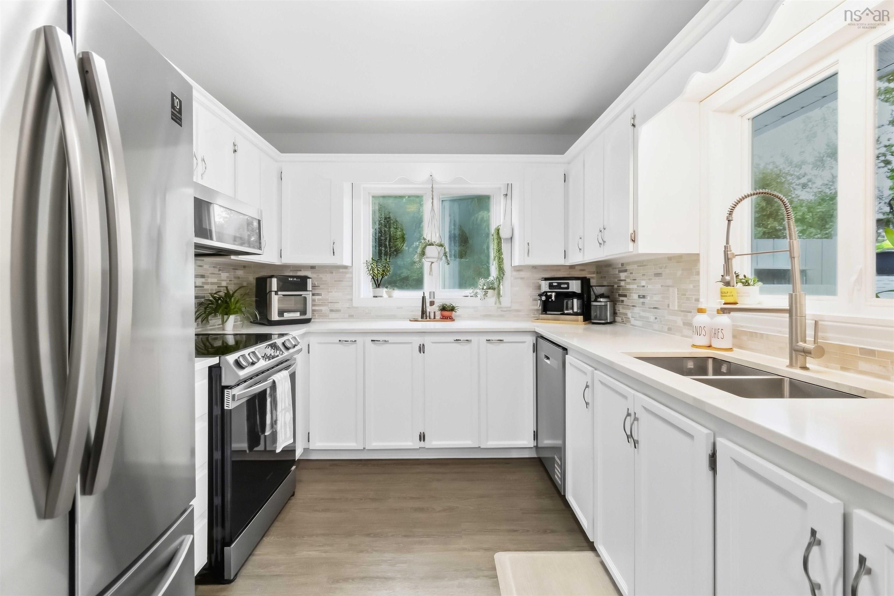 34 Lindsay Court, Lower Sackville, NS (MLS® 202624063) — U-shaped kitchen featuring white cabinetry, stainless steel appliances, a double basin sink, light-toned countertops, and wood-finish flooring
