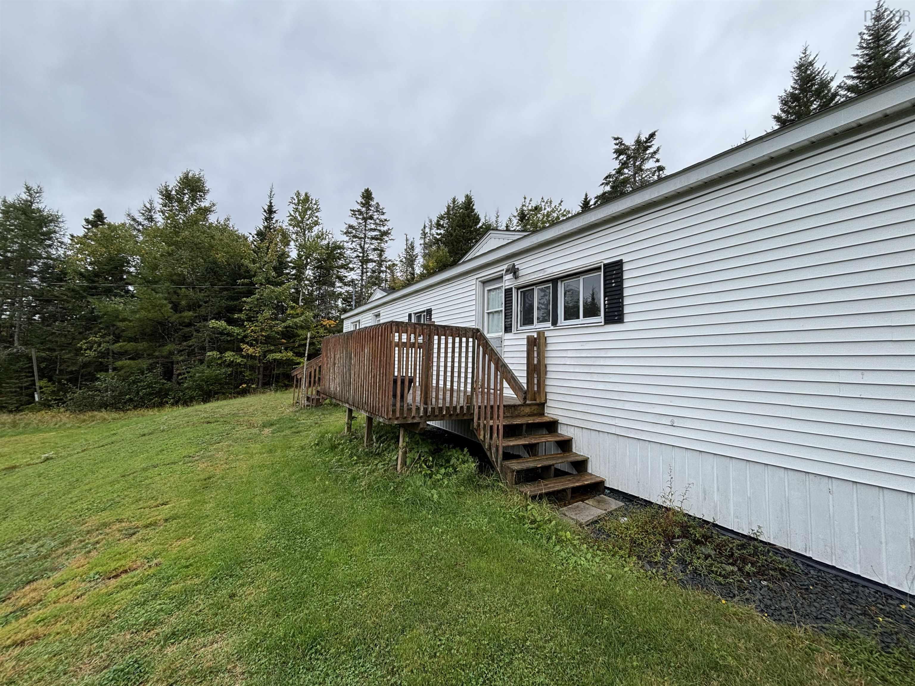 1126 Myra Road, Porters Lake, NS (MLS® 202624638) — White siding exterior with black window shutters, a wood deck, and a natural tree line backdrop
