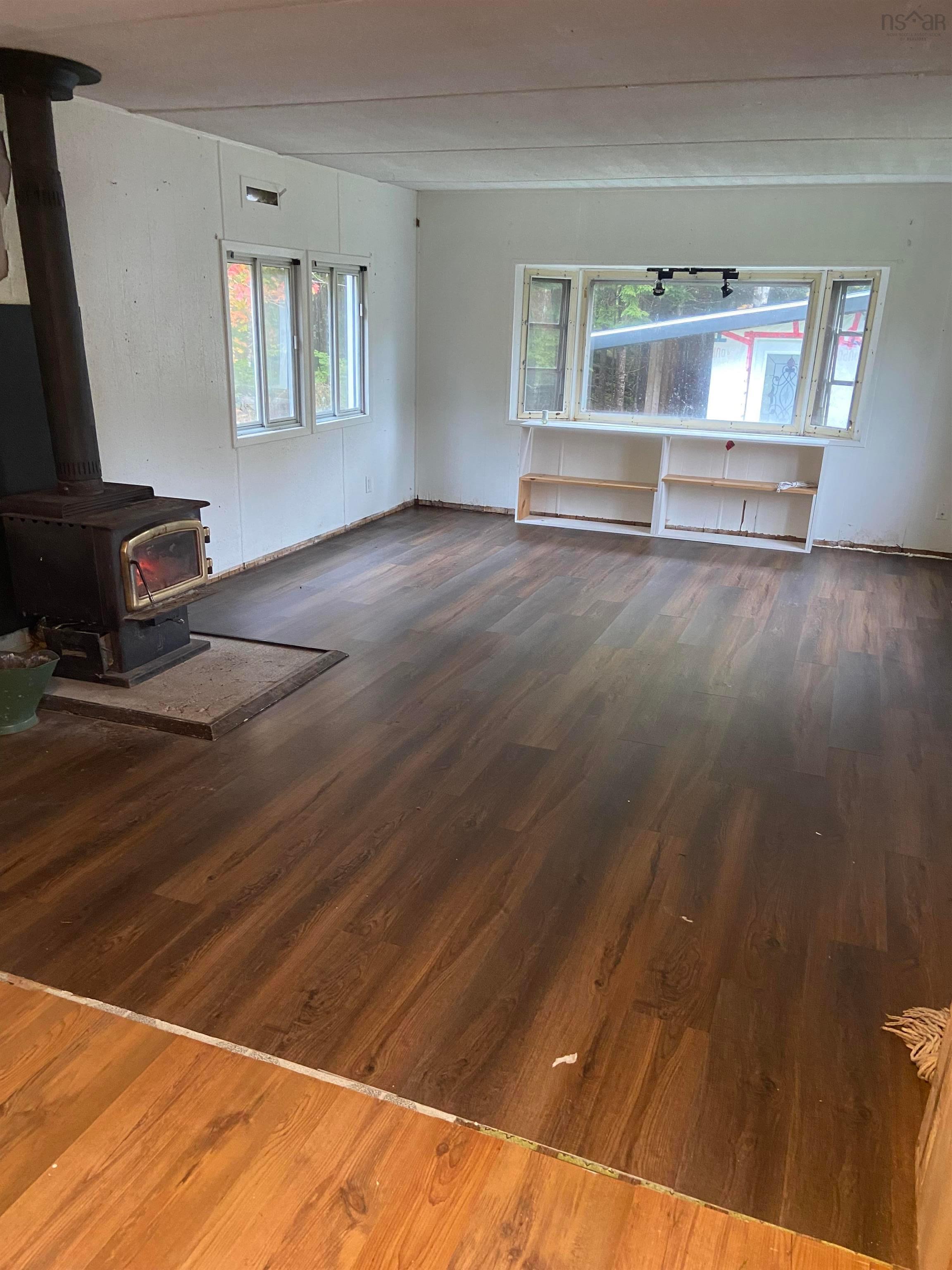 1126 Myra Road, Porters Lake, NS (MLS® 202624638) — Interior space featuring wood-finish flooring, a metal wood-burning stove, and dual windows