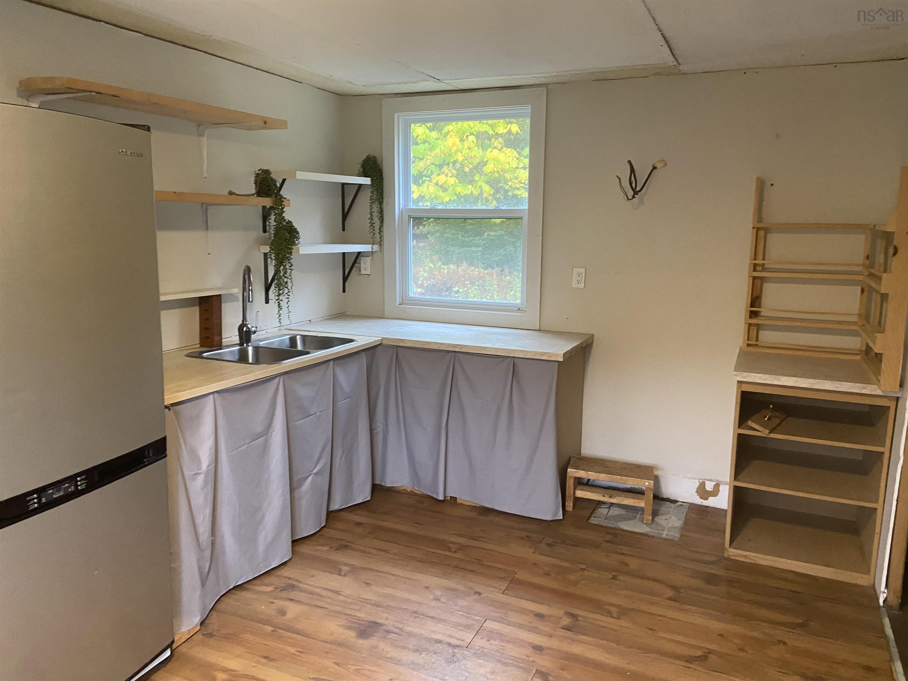 1126 Myra Road, Porters Lake, NS (MLS® 202624638) — Kitchen featuring wood-finish flooring, a stainless steel refrigerator, dual-basin stainless steel sink with high-arc faucet, open wood shelving, and built-in wood cabinetry