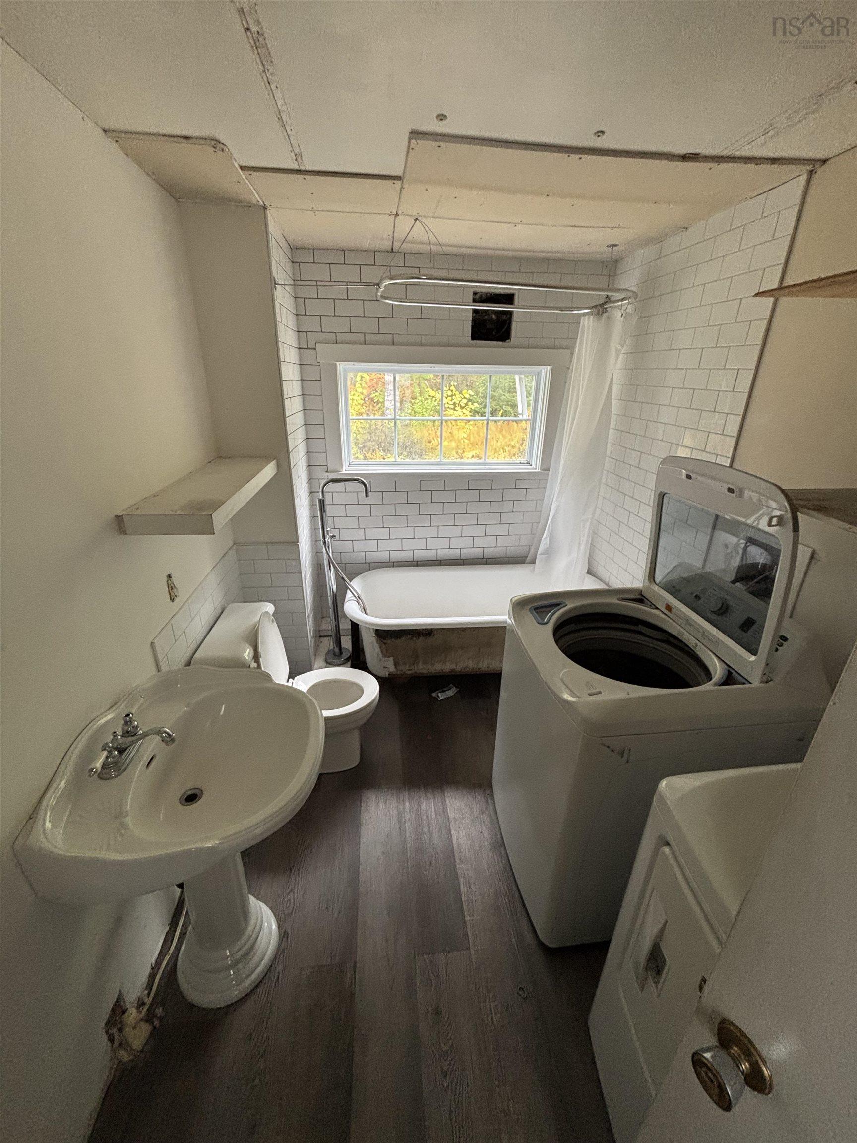 1126 Myra Road, Porters Lake, NS (MLS® 202624638) — Pedestal sink, white subway tile surround, window, clawfoot bathtub, and wood-finish flooring