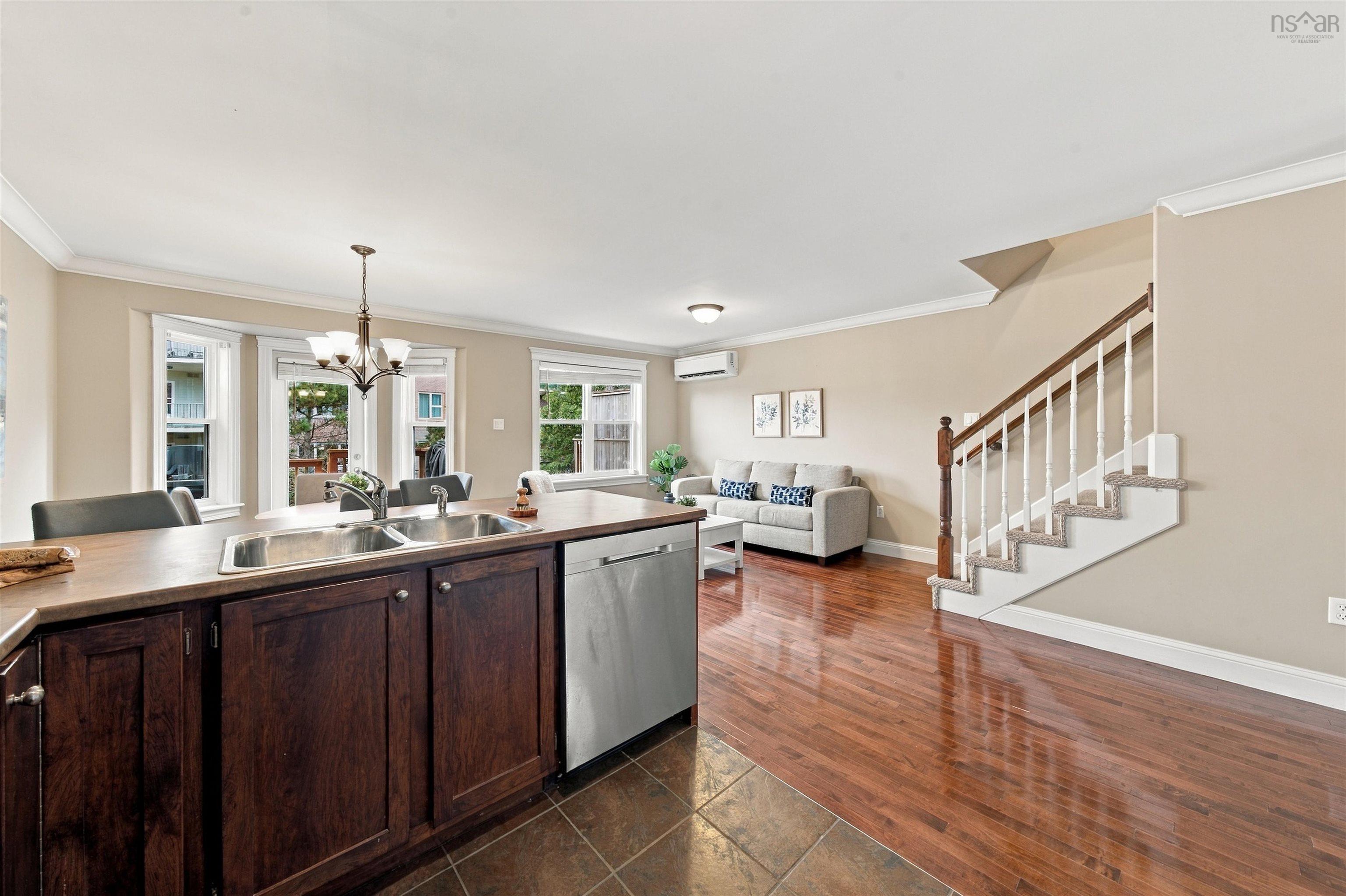 150 Transom Drive, Halifax, NS (MLS® 202625460) — Open-concept living area featuring rich wood-finish flooring, a kitchen island with dark wood cabinetry and a double basin sink, and a staircase with white spindles and a wood handrail