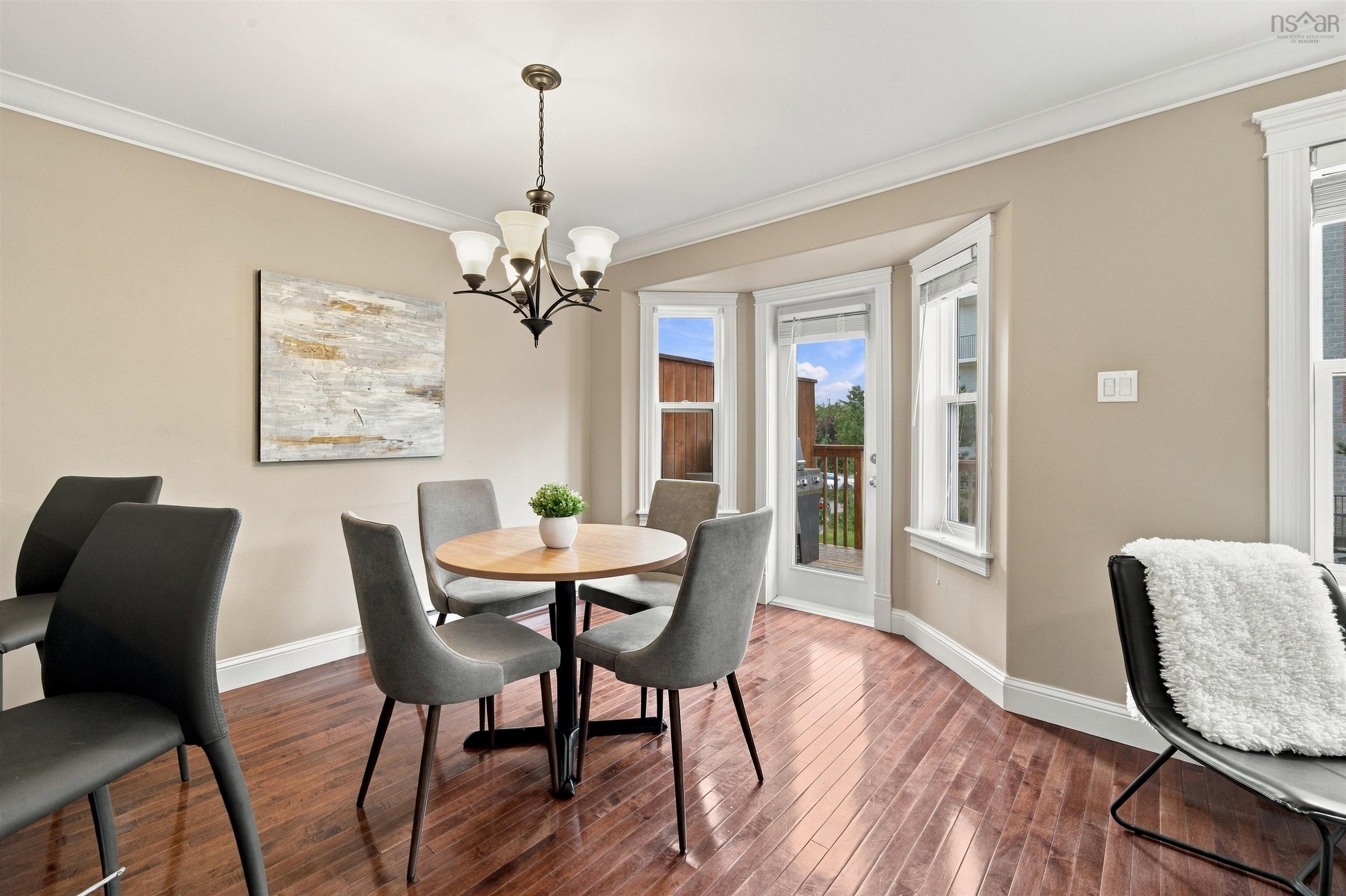 150 Transom Drive, Halifax, NS (MLS® 202625460) — Bright dining area featuring hardwood flooring, a round wood table with black base, upholstered dining chairs, and a black metal chandelier with frosted glass shades