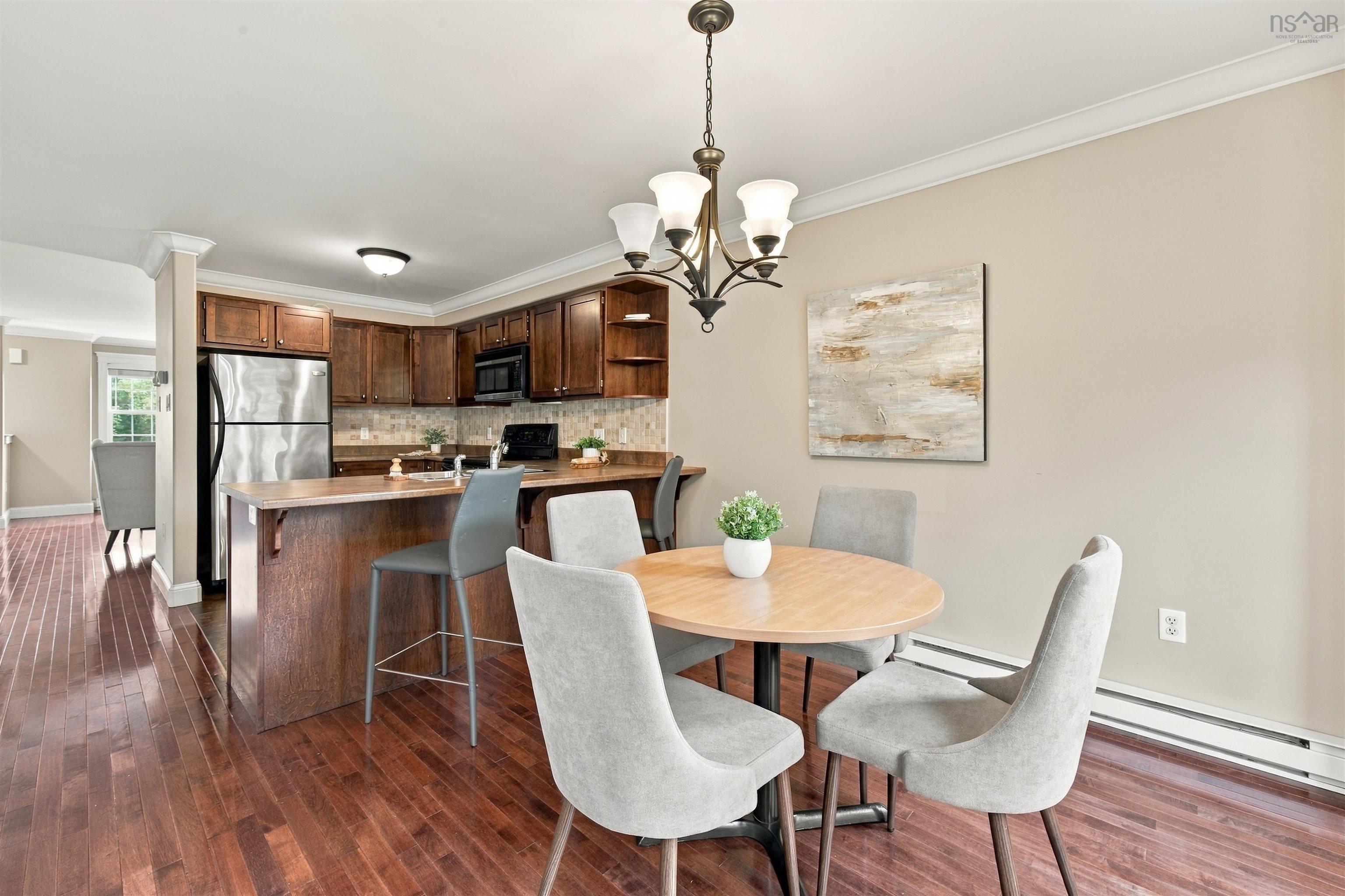 150 Transom Drive, Halifax, NS (MLS® 202625460) — Open-concept dining and kitchen area featuring a wood-finish dining table, upholstered chairs, wood cabinetry with stainless steel appliances, pendant lighting, and hardwood flooring throughout