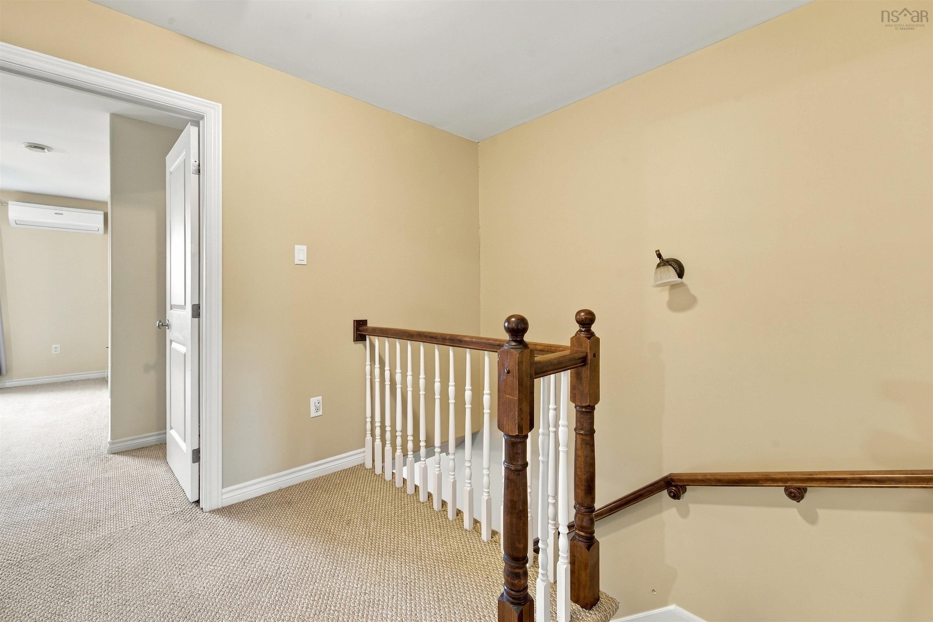 150 Transom Drive, Halifax, NS (MLS® 202625460) — Hallway featuring warm yellow walls, white-trimmed doorway leading to additional spaces, decorative wooden stair railing with turned balusters, and neutral carpet flooring throughout