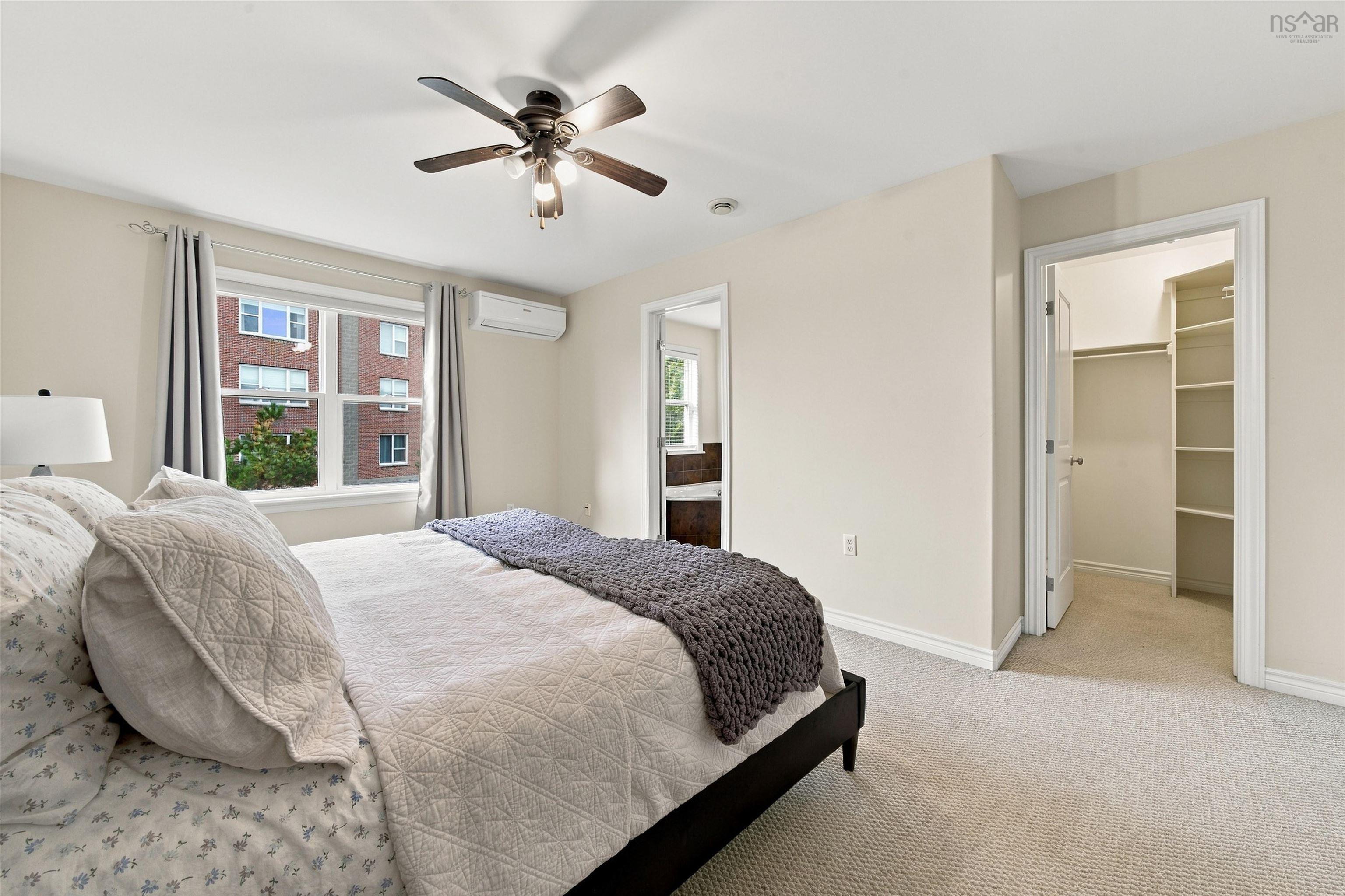 150 Transom Drive, Halifax, NS (MLS® 202625460) — Spacious primary bedroom featuring neutral wall finishes, carpeted flooring, ceiling fan with integrated lighting, dual closets with sliding doors, and large windows with thermal-lined curtains overlooking neighborhood streetscape