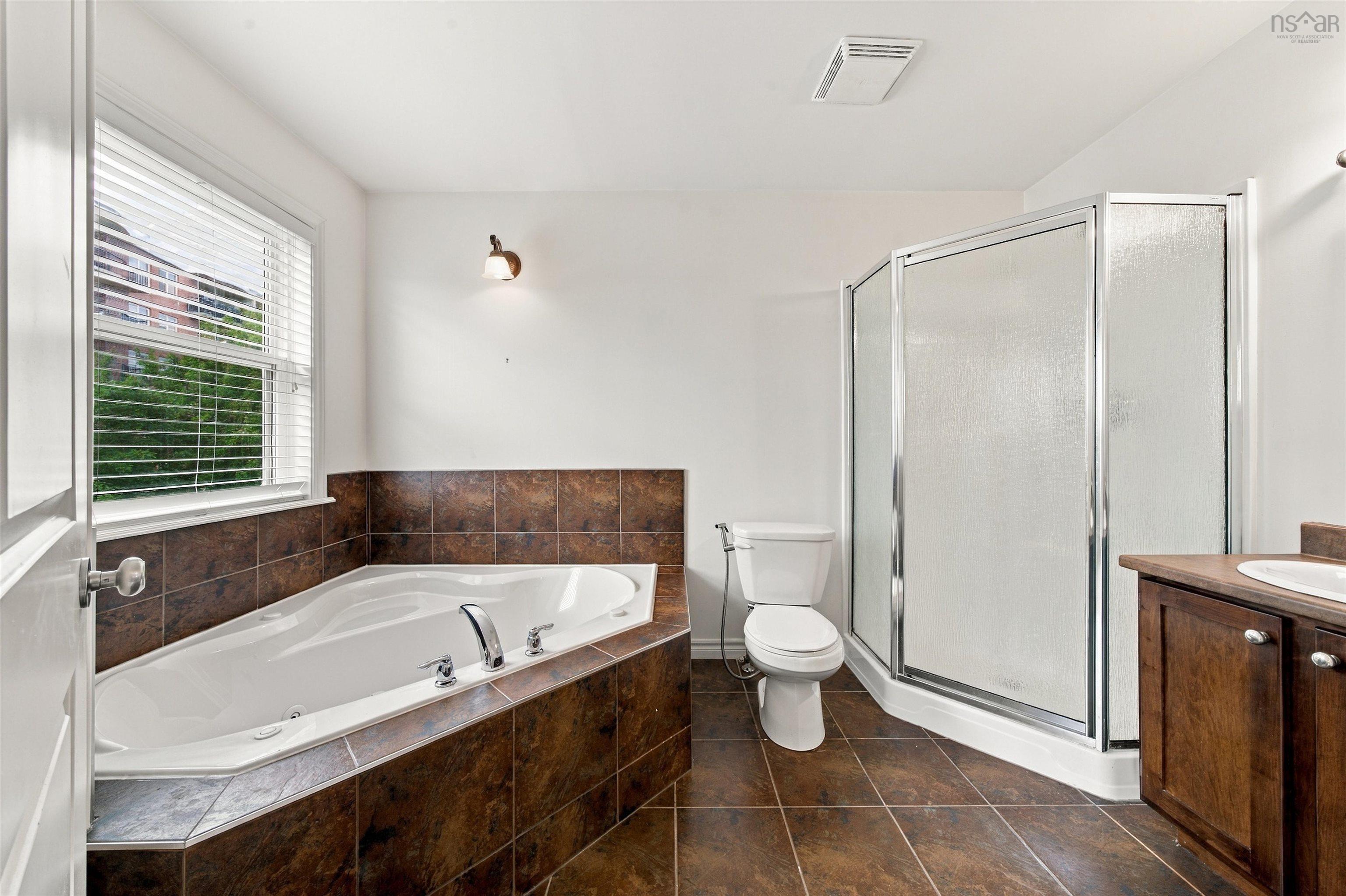150 Transom Drive, Halifax, NS (MLS® 202625460) — Corner soaking tub, separate glass-enclosed shower, single vanity with wood-finish cabinetry, ceramic tile flooring, and a window with blinds