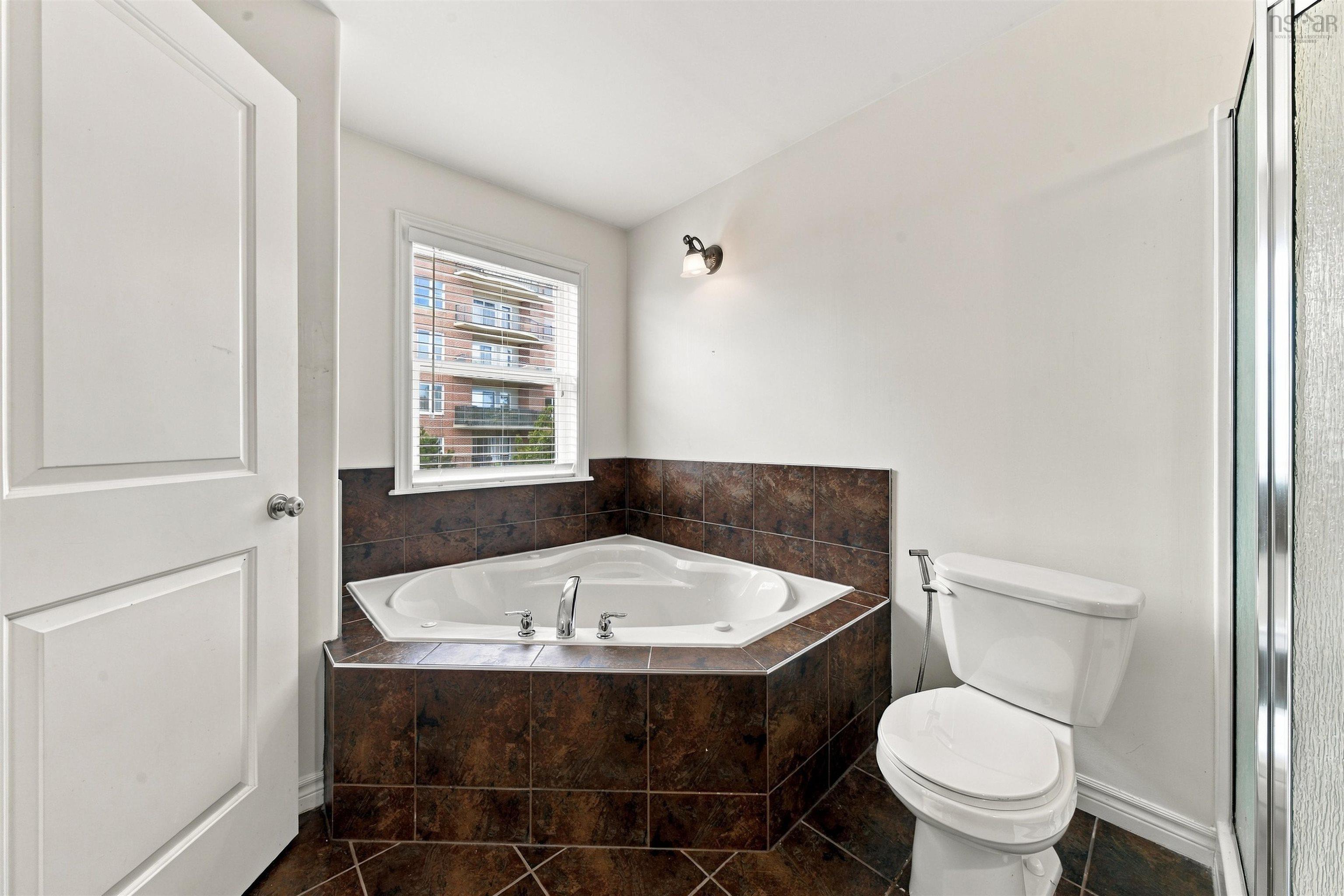 150 Transom Drive, Halifax, NS (MLS® 202625460) — Corner soaking tub with tile surround, white toilet, and walk-in shower with clear glass enclosure