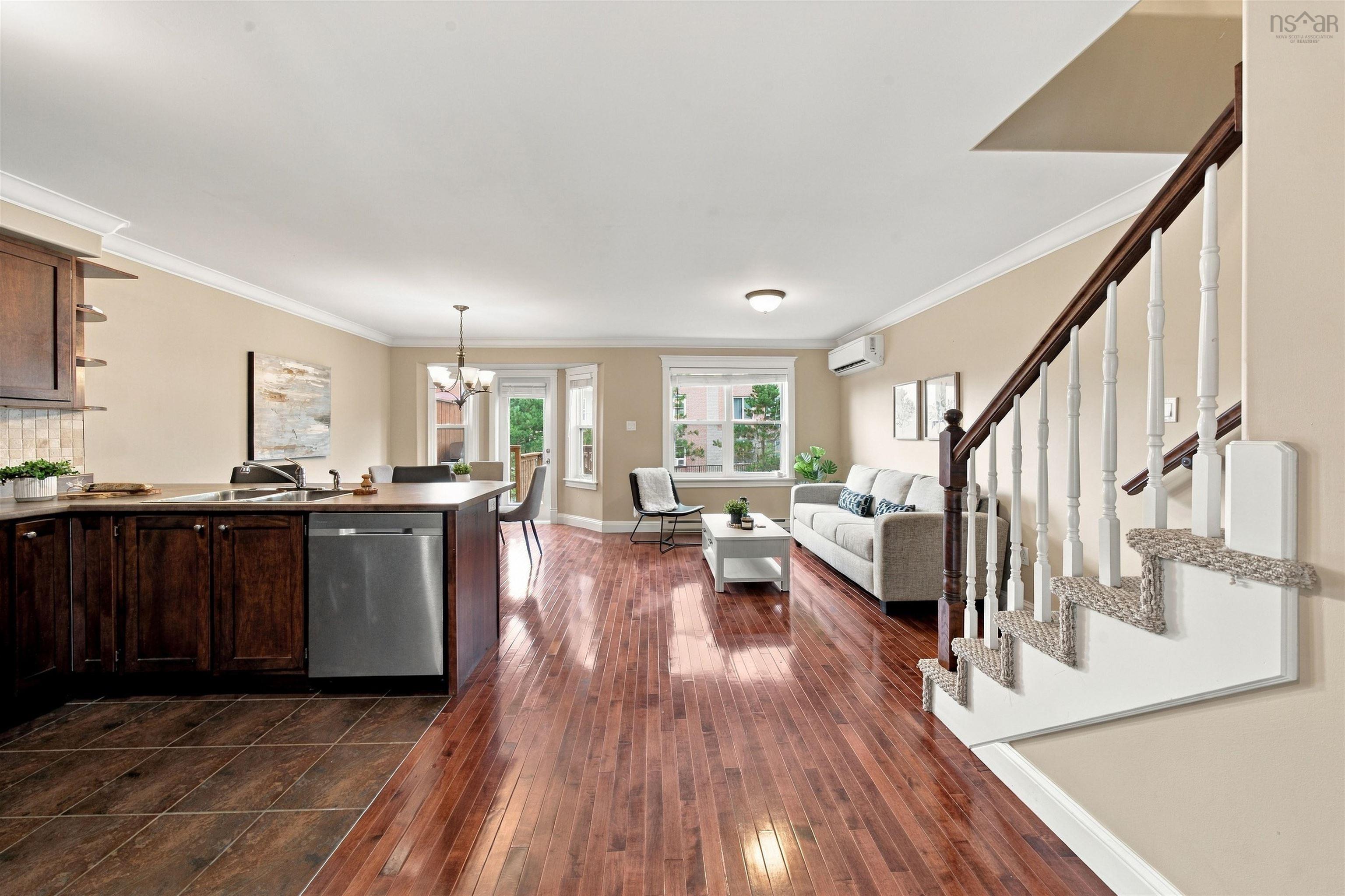 150 Transom Drive, Halifax, NS (MLS® 202625460) — Open-concept living area featuring rich wood-finish flooring, a kitchen island with seating, dark wood cabinetry, and a carpeted staircase with white balusters