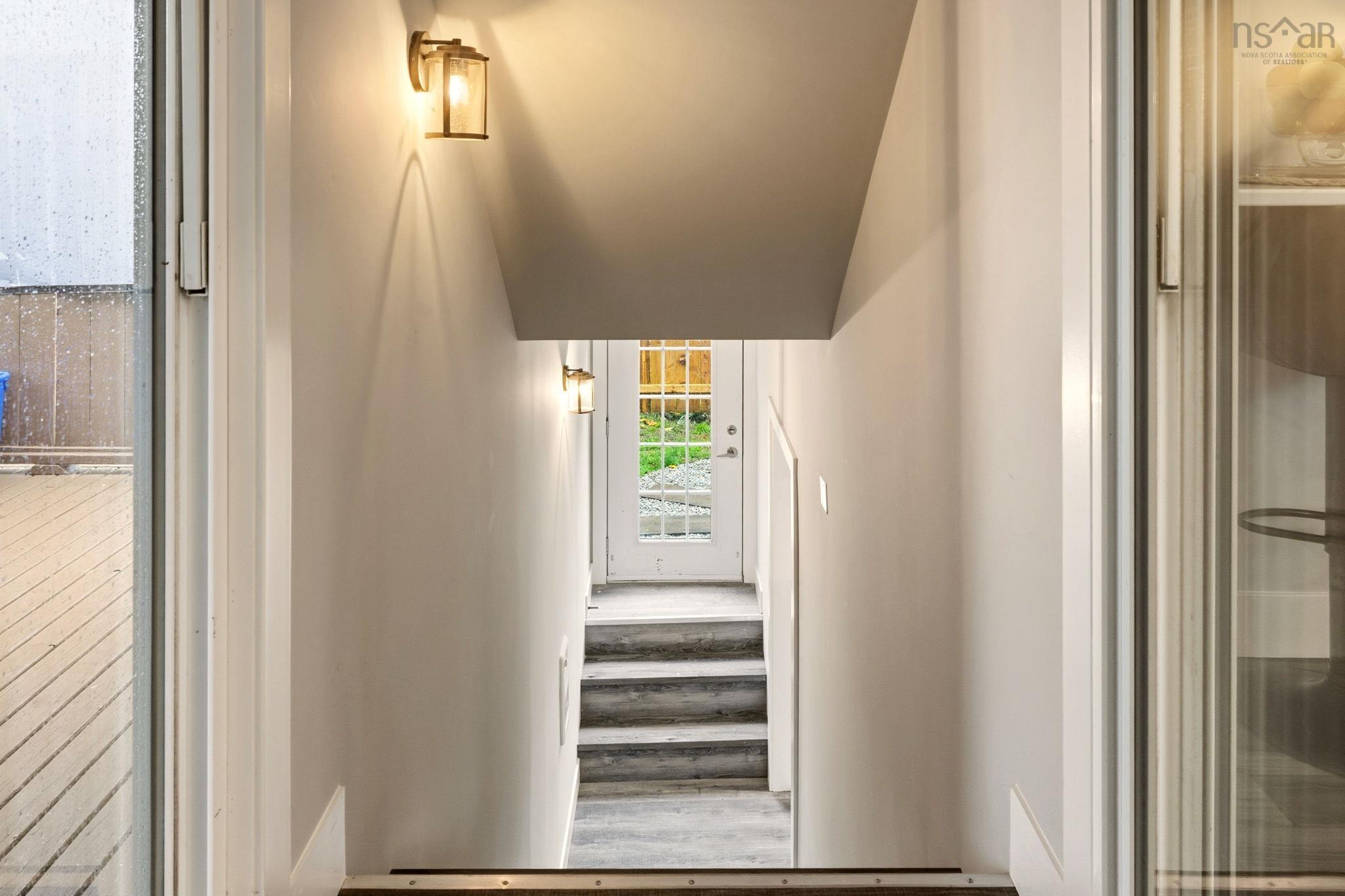 25 Circle Drive, Halifax, NS (MLS® 202625881) — Stairway featuring wood-finish flooring, white walls, and two wall-mounted metallic fixtures, terminating at a white-framed glass-panel door