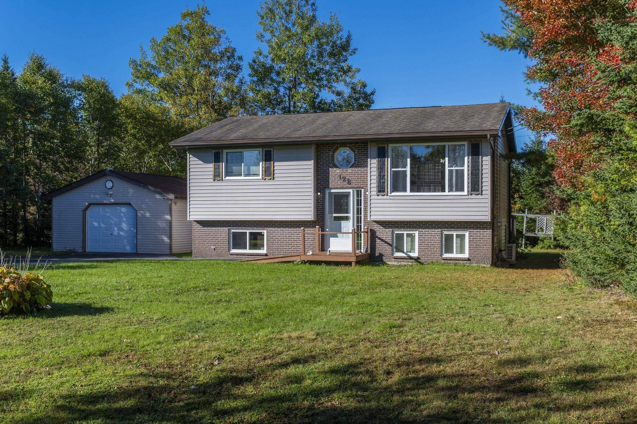 128 Doherty Drive, Lawrencetown, NS (MLS® 202625891) — Split-level exterior featuring light-toned vinyl siding, brick masonry lower level, detached single-car garage, and a wood-deck entryway
