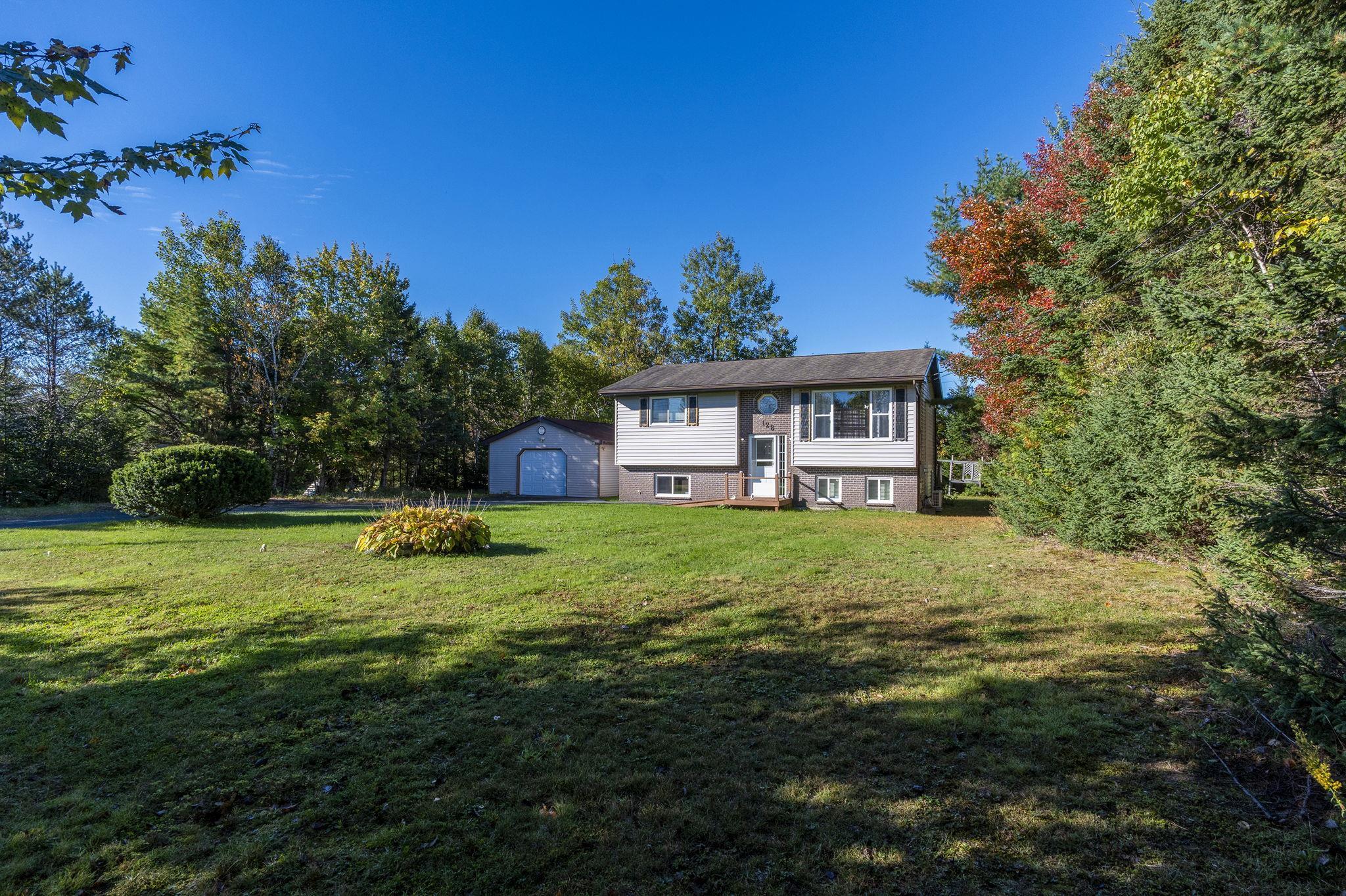 128 Doherty Drive, Lawrencetown, NS (MLS® 202625891) — Split-level exterior featuring light-toned horizontal siding, a detached garage, and a spacious front lawn bordered by mature trees