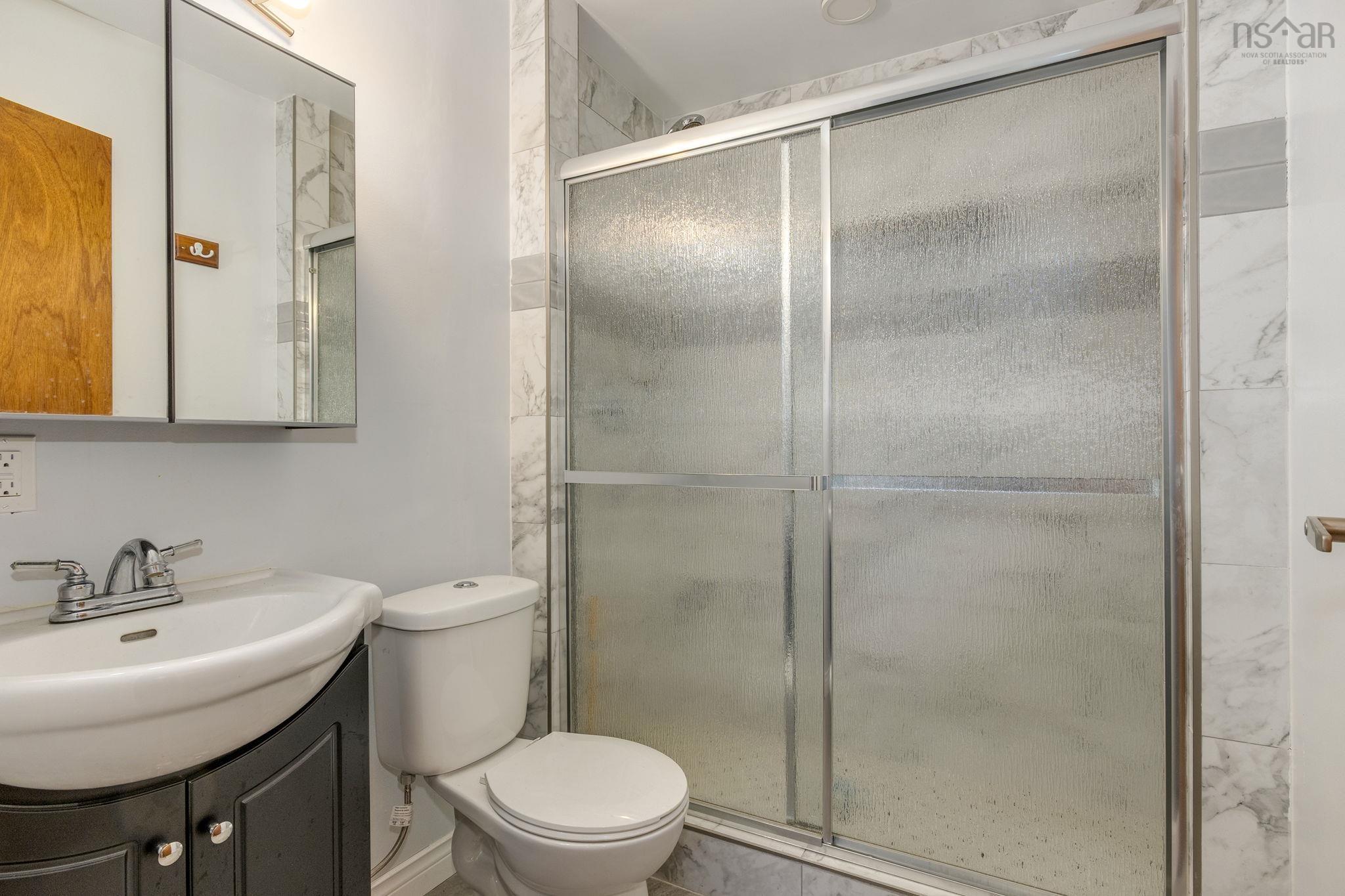 128 Doherty Drive, Lawrencetown, NS (MLS® 202625891) — Bathroom featuring a shower with a sliding glass door and stone-patterned wall tile, a dark-finish vanity cabinet, a drop-in sink, and a mirrored medicine cabinet