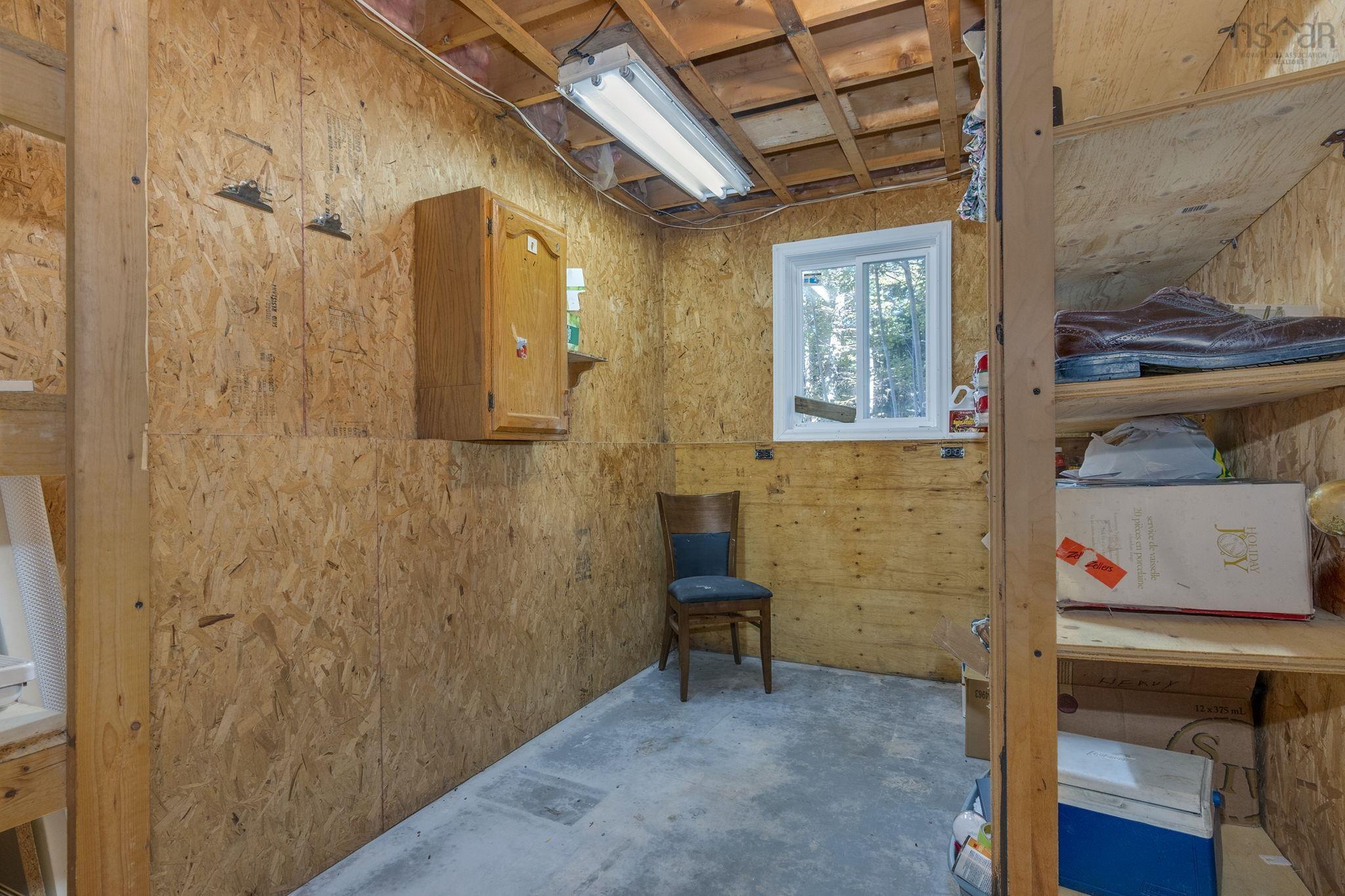 128 Doherty Drive, Lawrencetown, NS (MLS® 202625891) — Utility space featuring oriented strand board (OSB) wall paneling, concrete flooring, built-in wooden shelving, a wall-mounted wooden cabinet, and a single-pane window