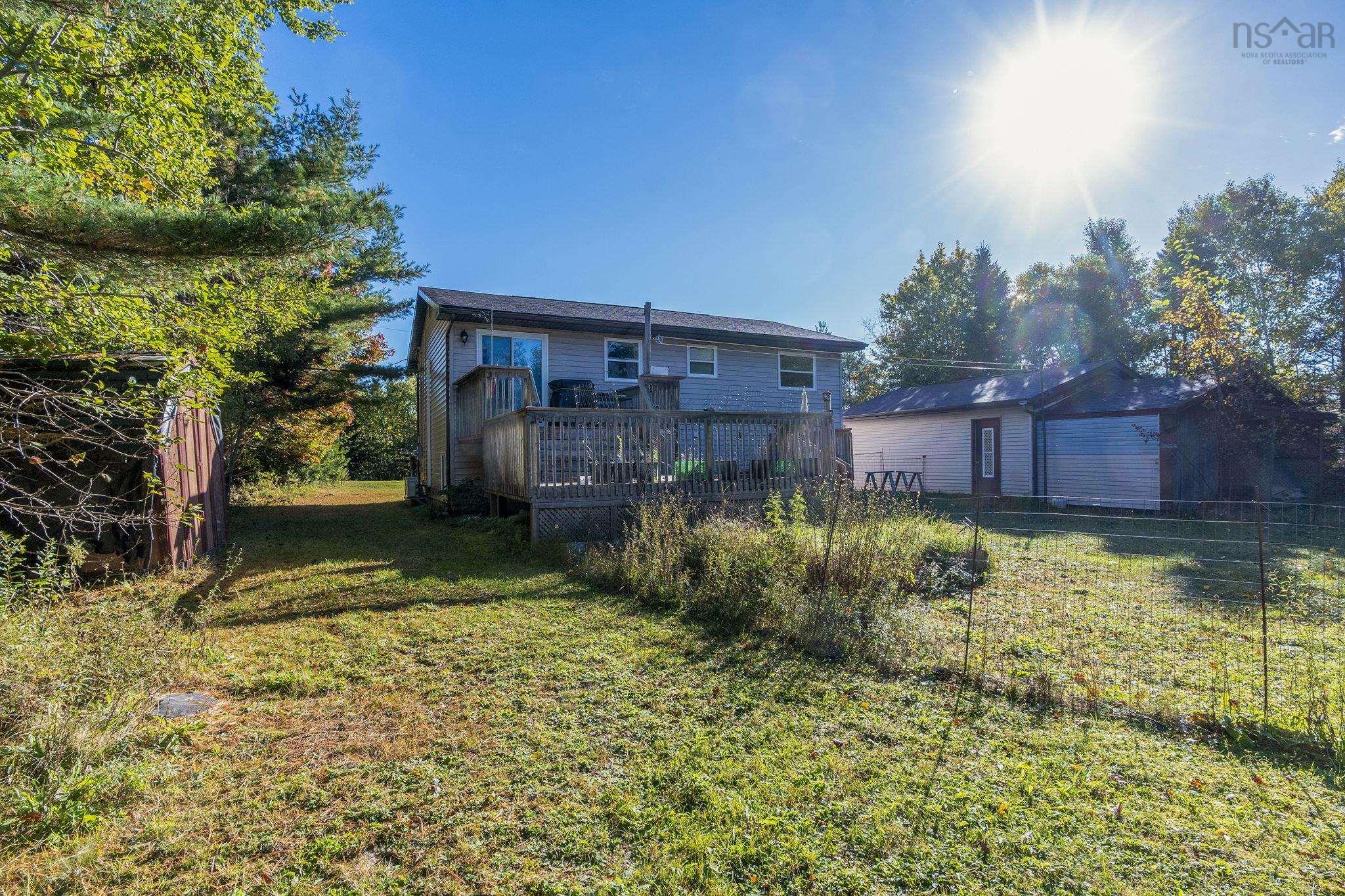 128 Doherty Drive, Lawrencetown, NS (MLS® 202625891) — Rear exterior featuring a multi-level wood deck, light-toned horizontal siding, and a detached structure with an integrated garage