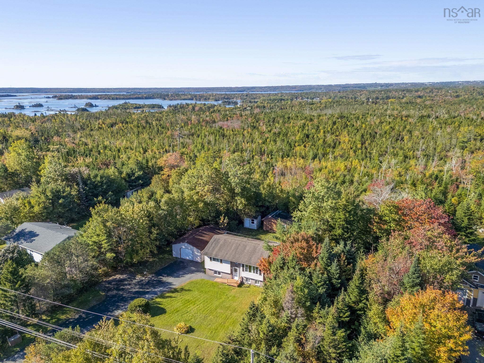 128 Doherty Drive, Lawrencetown, NS (MLS® 202625891) — Detached residential property featuring a pitched roof, attached garage, paved driveway, and manicured lawn, situated on a large, wooded lot with coastal water scenery in the distance