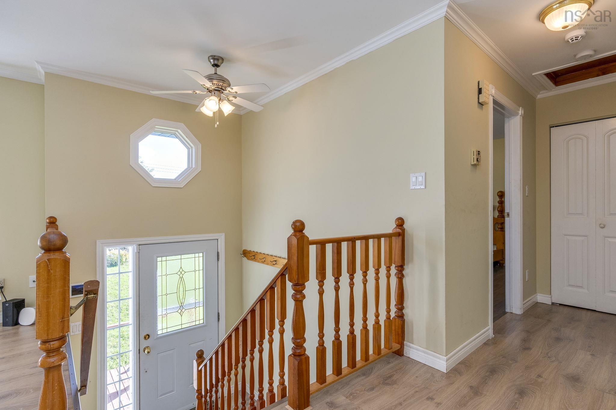 128 Doherty Drive, Lawrencetown, NS (MLS® 202625891) — Entryway featuring wood-finish flooring, a decorative octagon window, an exterior door with leaded glass insert, a wood stair railing with turned balusters, and crown molding