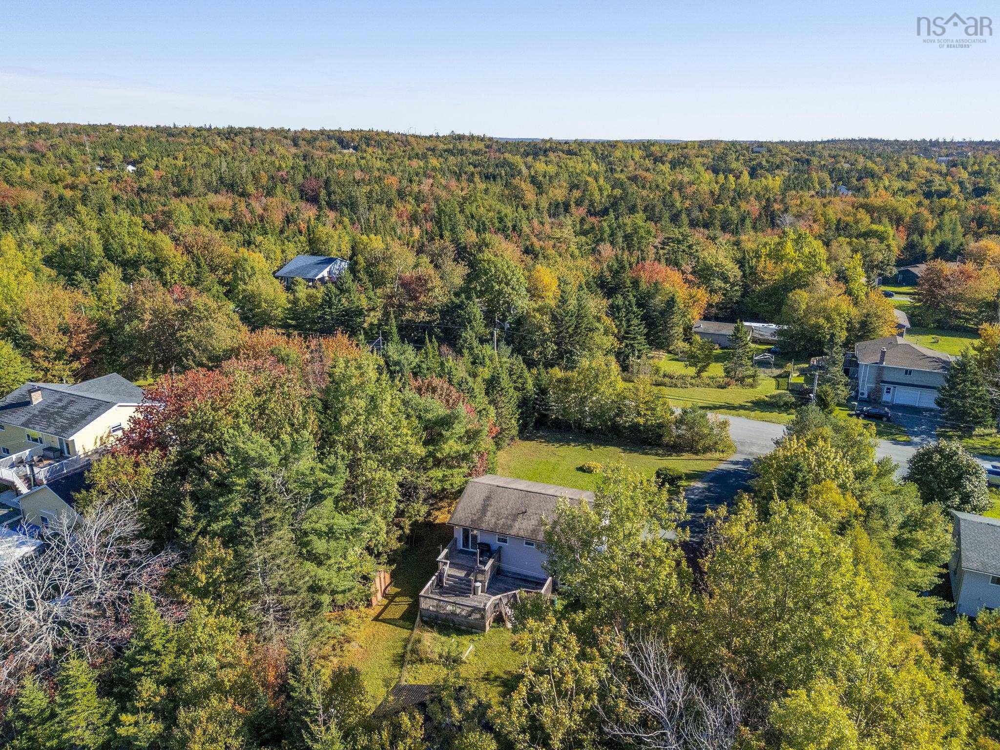 128 Doherty Drive, Lawrencetown, NS (MLS® 202625891) — Aerial view of a residential property featuring a detached house with a multi-level rear deck, an asphalt driveway, and extensive perimeter foliage