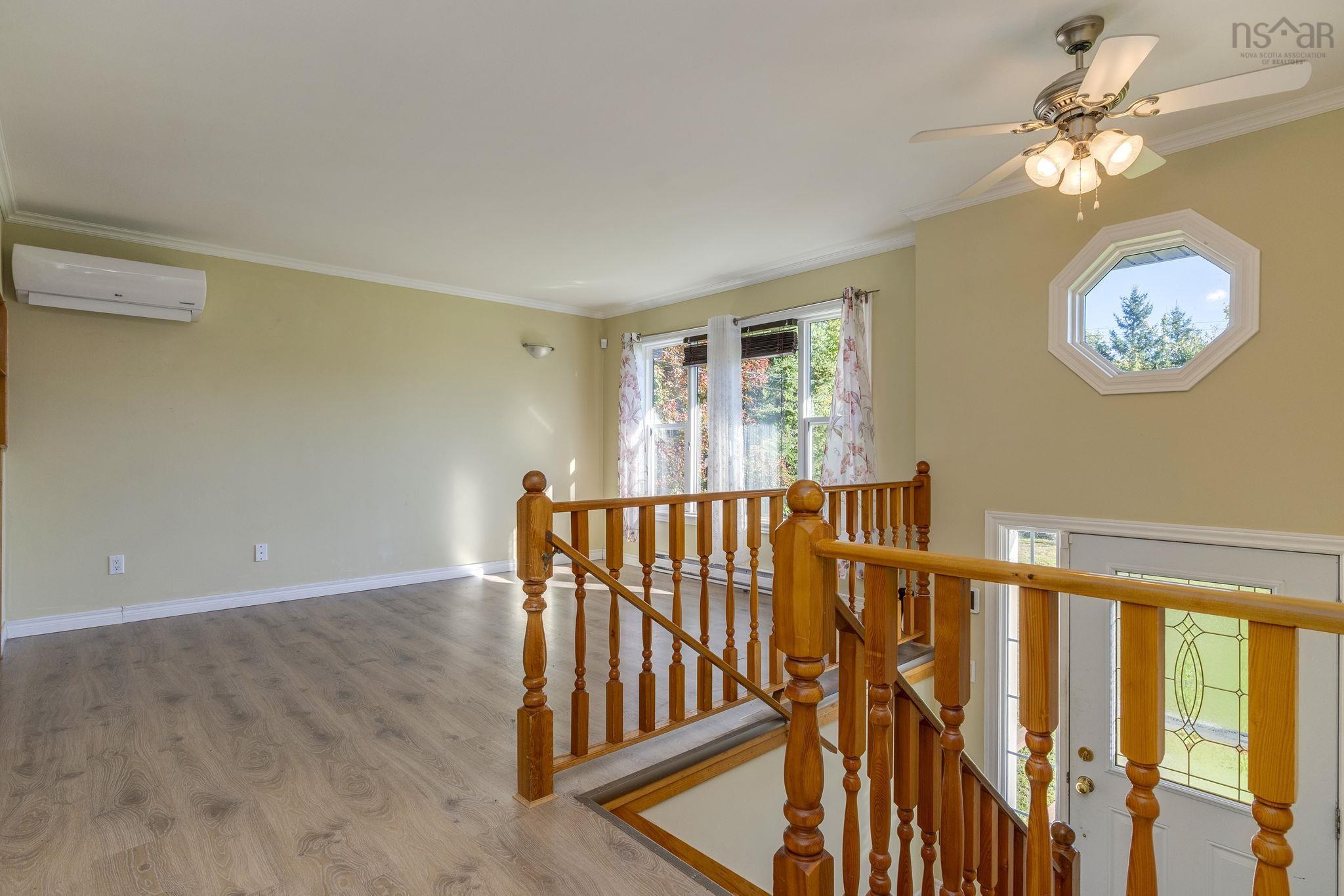 128 Doherty Drive, Lawrencetown, NS (MLS® 202625891) — Wood-finish flooring, wall-mounted ductless climate control unit, octagon-shaped window, ceiling fan with integrated lighting, and wooden staircase railing